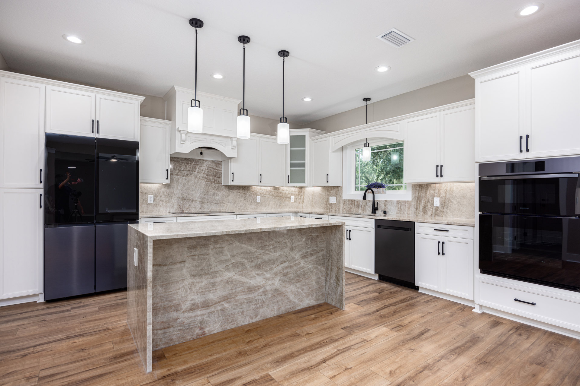 Marble kitchen island with waterfall edge, black appliances, wood flooring, white cabinetry, stainless steel oven, undermount sink, and neutral walls