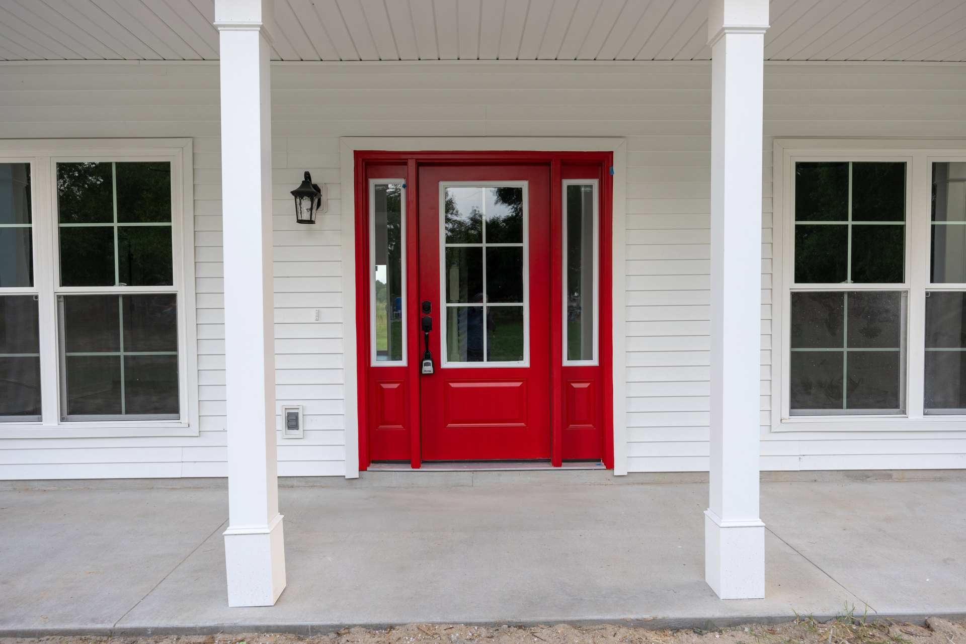 Red front door with glass panes set in white siding, adjacent to a window with a white frame.