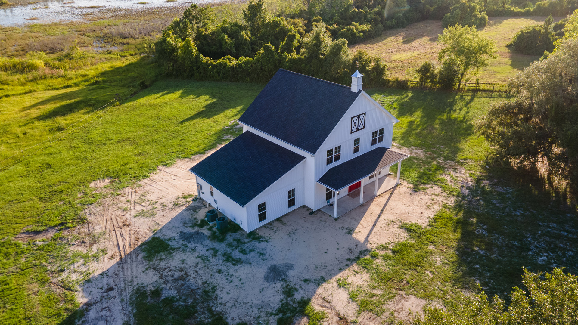 White siding house with blue metal roof, red front door, grassy lawn, small trees, and shrubs in front yard