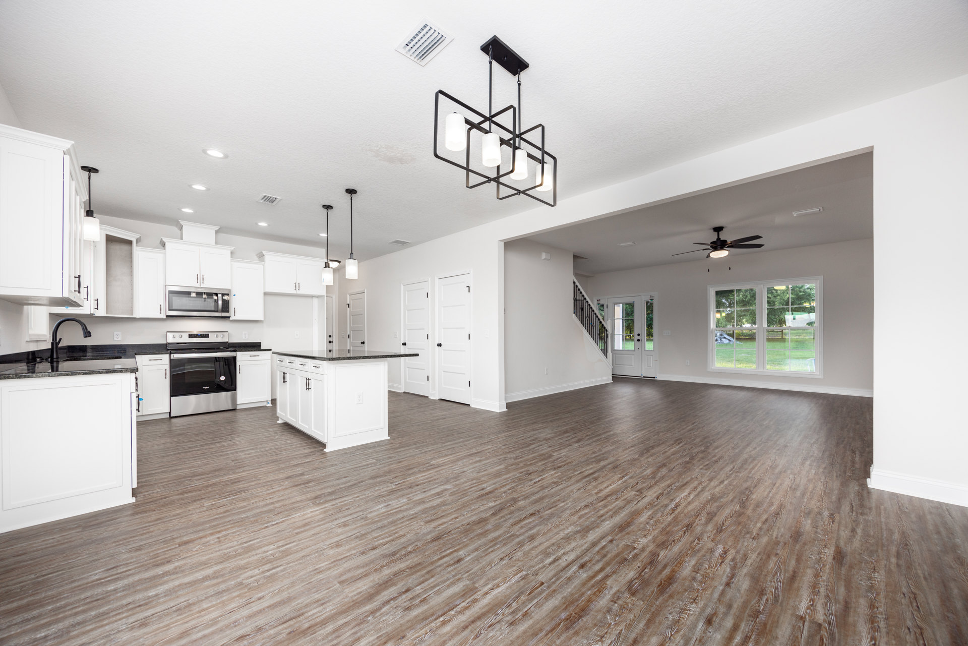 Spacious kitchen with white walls, wood laminate flooring, ceiling fan, open oven door, white cabinetry, and window overlooking green lawn