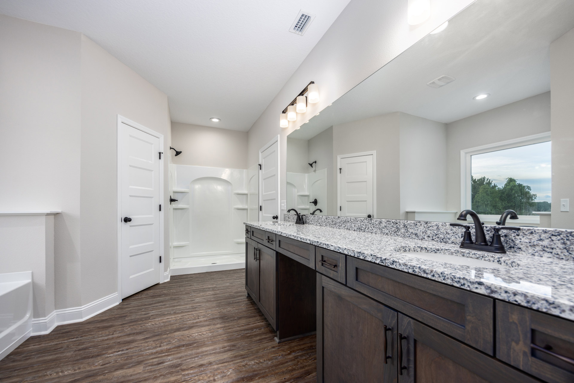 Bathroom with marble countertop, undermount sink, white cabinetry, glass-enclosed shower, white walls, black hardware, window with view of trees