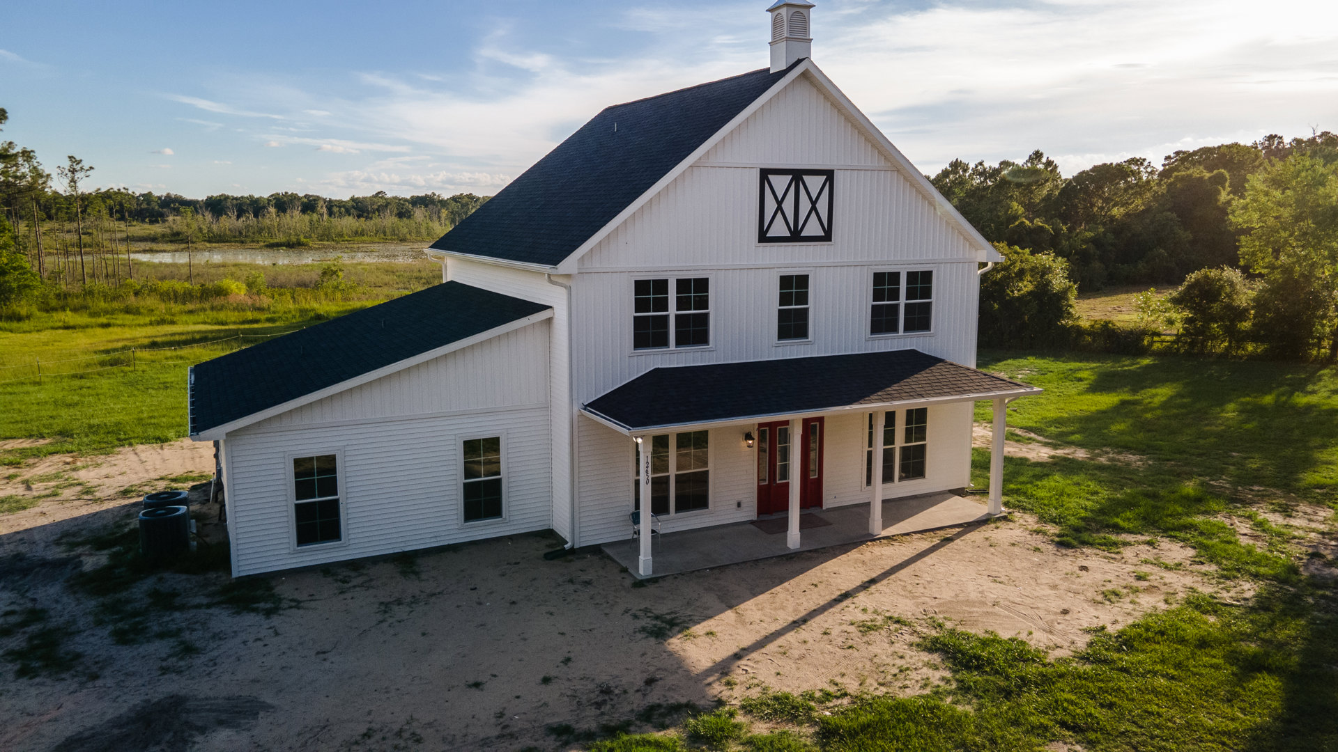 White siding house with black shingle roof, rectangular windows, grassy lawn, and trees in background