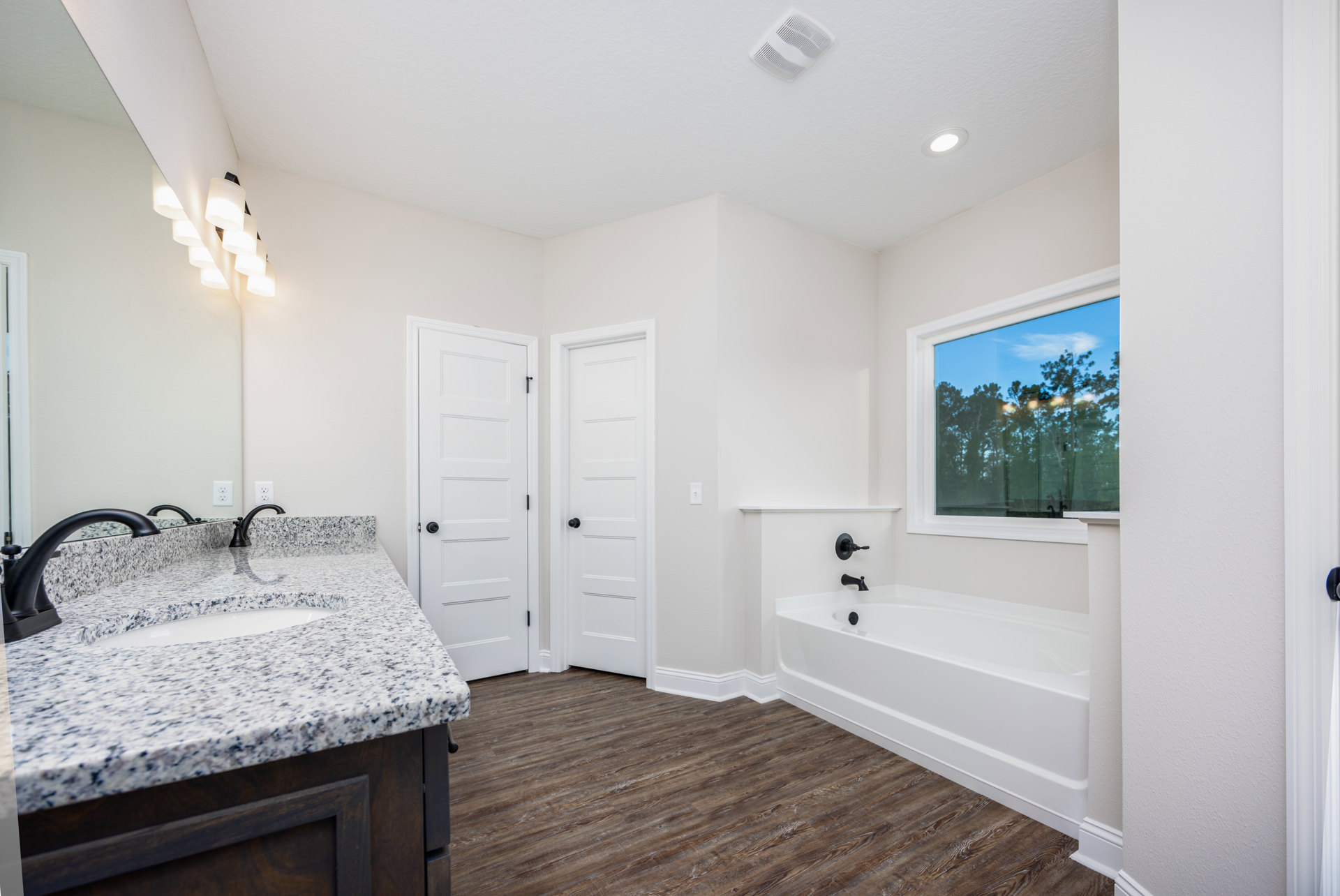 Bathroom featuring a freestanding white bathtub with matte black faucet, white vanity with integrated sink and black faucet, large window overlooking trees, white door with black