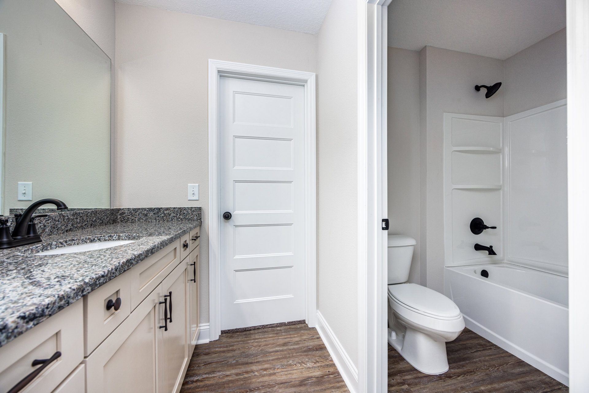 Bathroom with white toilet, marble countertop, black faucet, black shower head, white door with black knob, and light tile walls