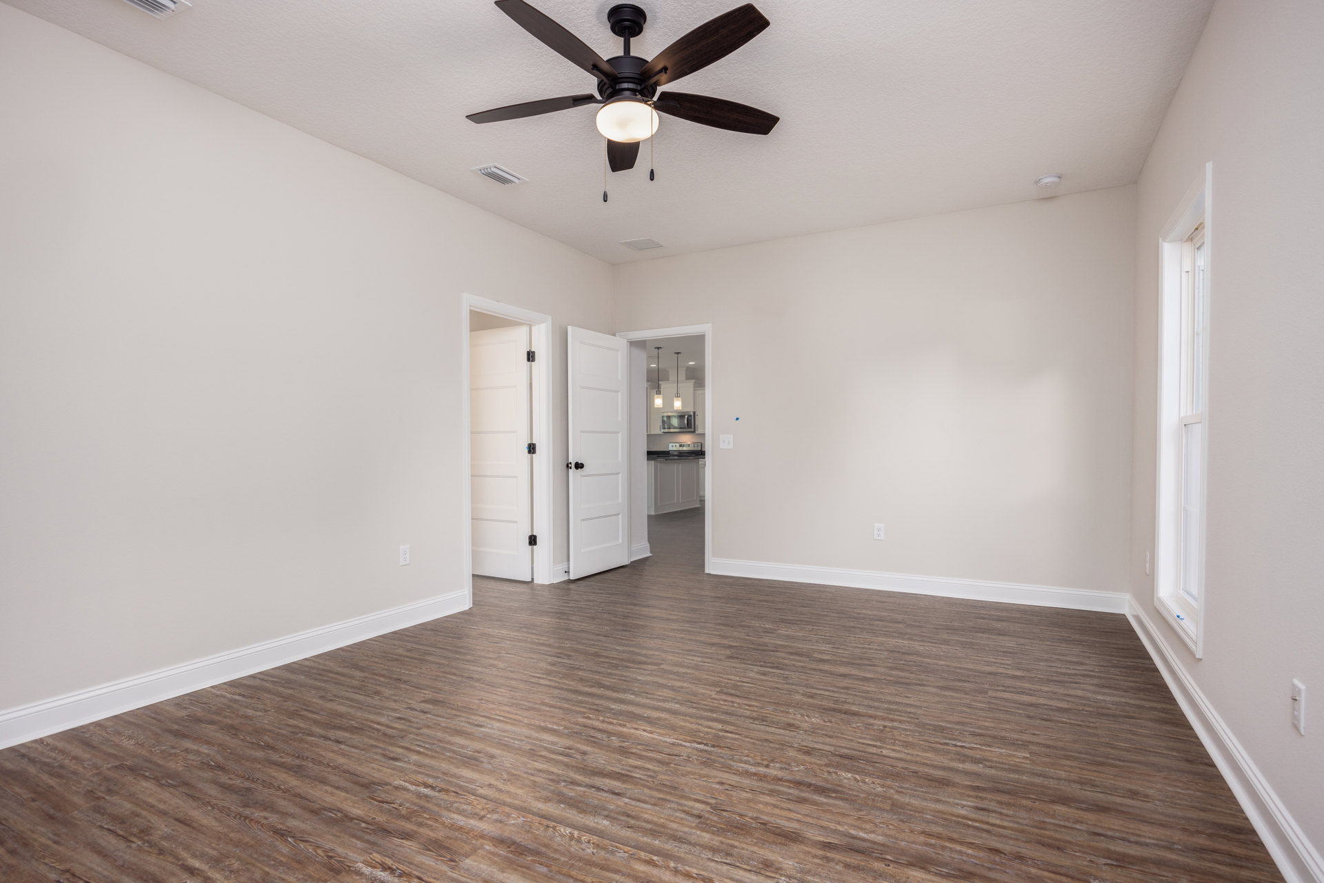 Ceiling fan with integrated light fixture mounted above wood flooring, white doors featuring black knobs and hinges, neutral plaster walls