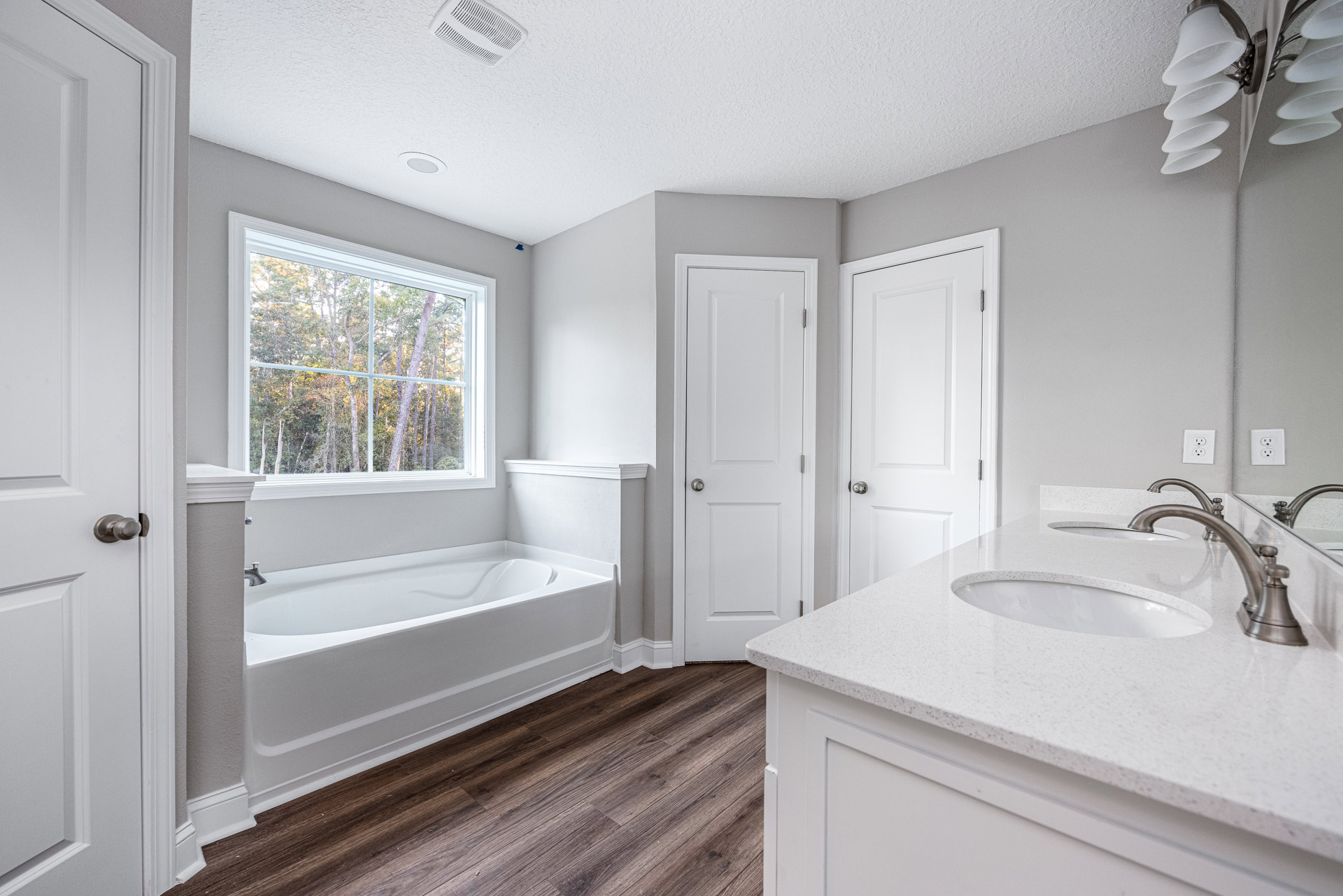 Bathroom with freestanding tub, white countertop sink, silver faucets, tiled walls, window overlooking trees, white door with silver doorknob, ceiling light fixture with white