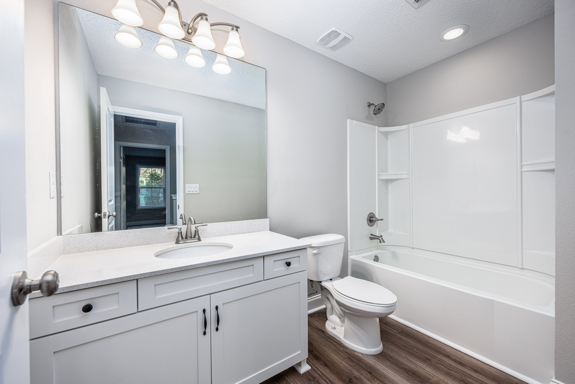 Bathroom with white sink, freestanding bathtub, white toilet, tiled walls, ceiling light fixture, and window with white frame