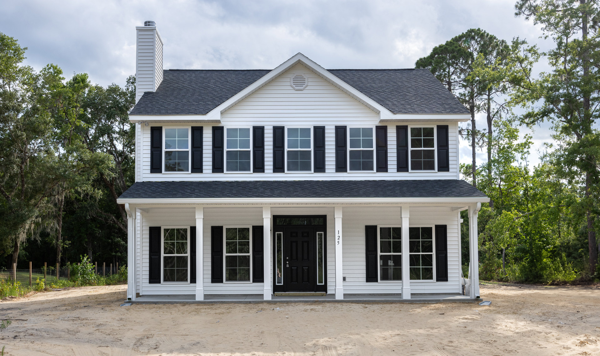 White siding exterior with black shutters, black front door featuring glass panes, white columns framing entry porch, white vent and window with white trim, landscaped yard with