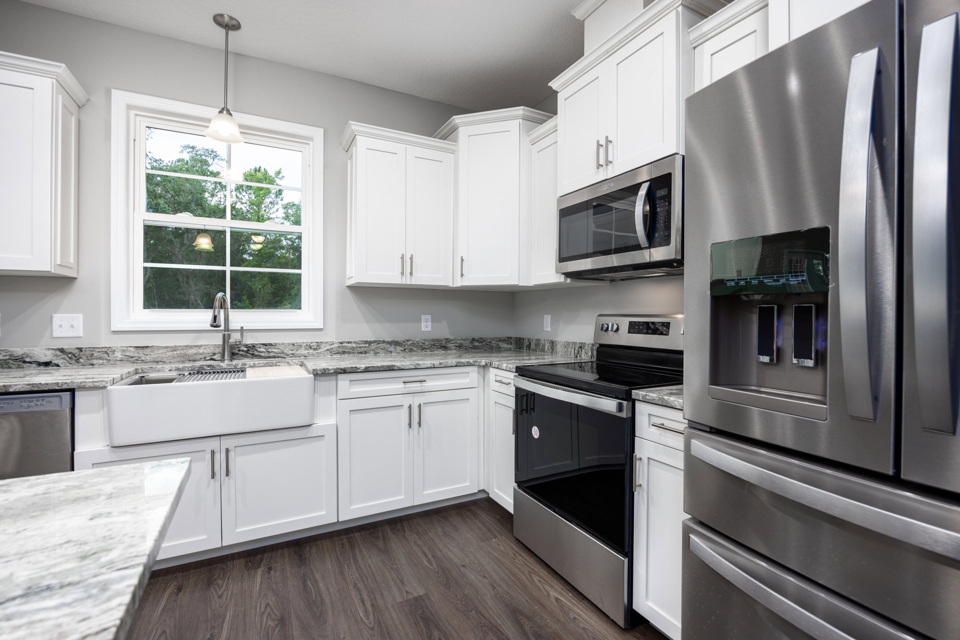 White shaker cabinets, stainless steel refrigerator and oven, built-in microwave, undermount sink beneath window, quartz countertops, brushed metal faucet