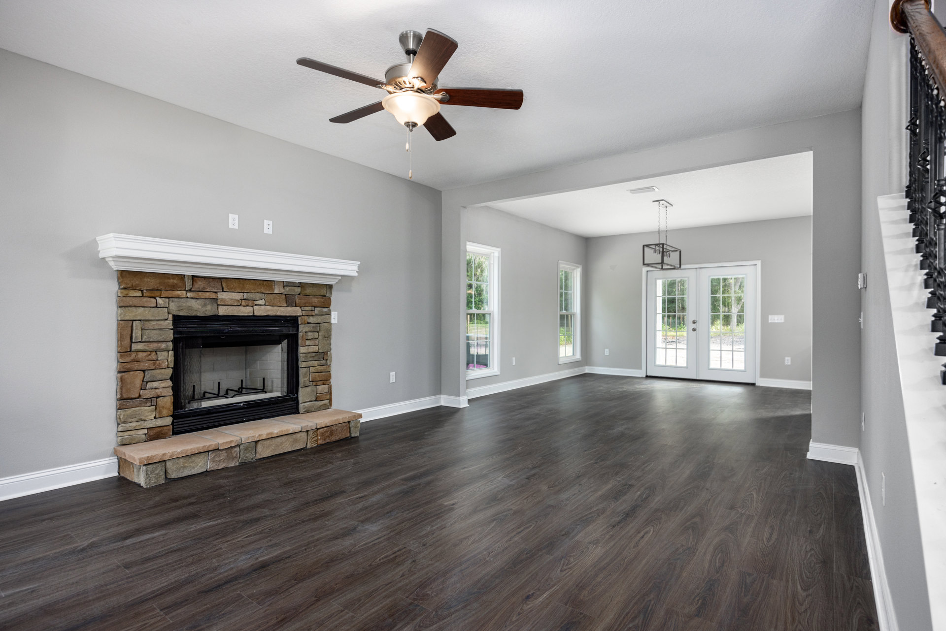 Living room with hardwood flooring, black-framed fireplace with mesh screen, ceiling fan with light fixture, and double glass-paneled doors