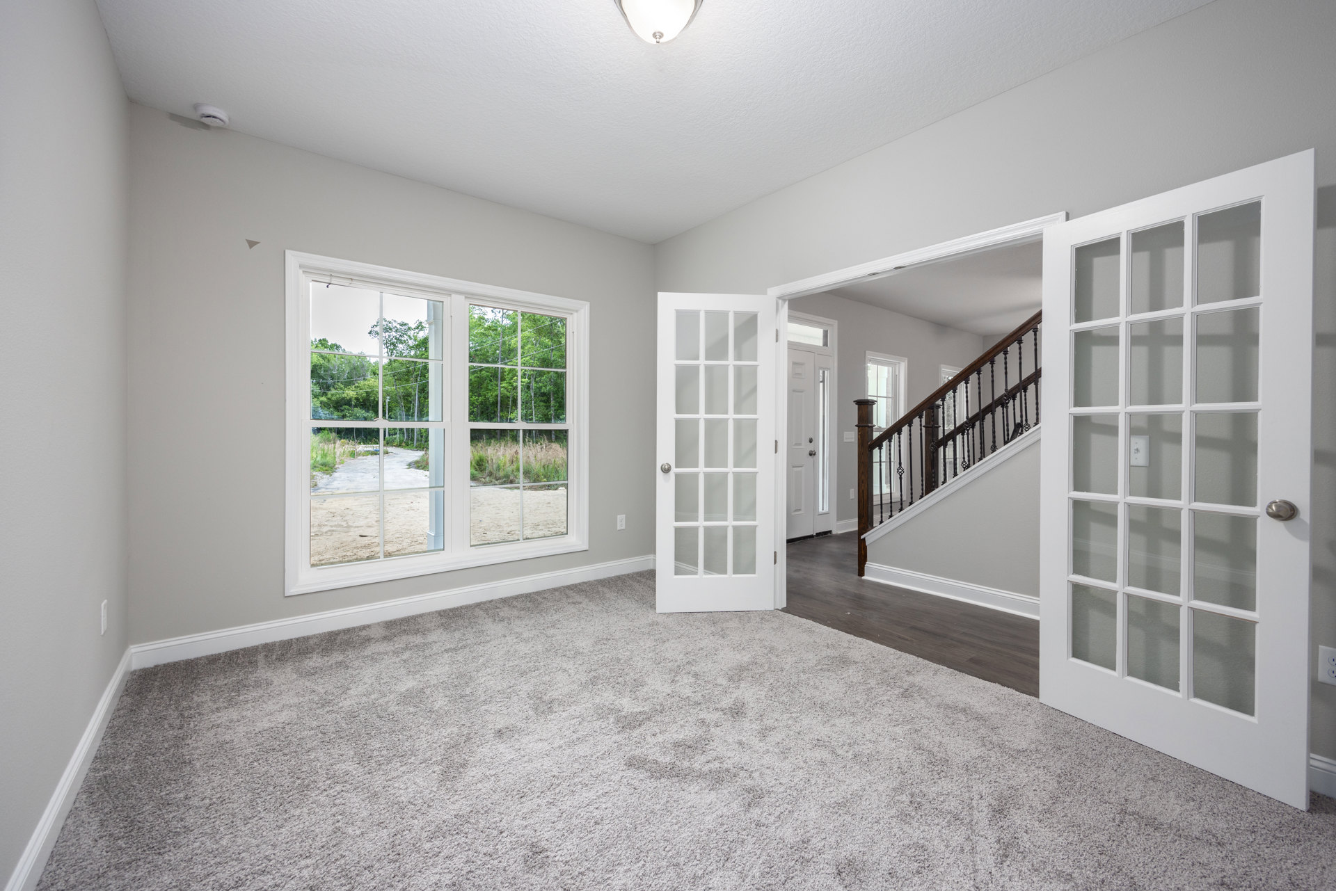 Open doorway leading to carpeted room with staircase featuring wooden railing, large window with glass panes, white plaster walls, and ceiling.
