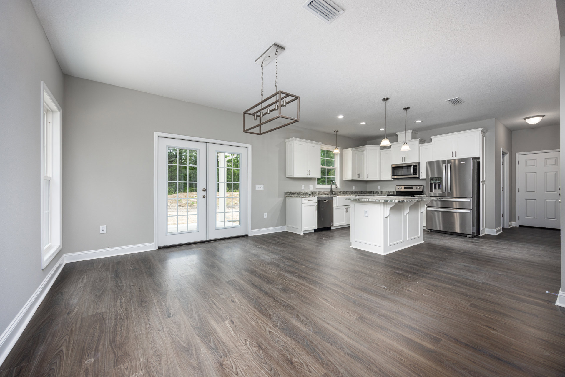 Open kitchen and dining area with hardwood flooring, stainless steel double-door refrigerator, white cabinetry with silver handles, built-in microwave, glass-paneled double doors