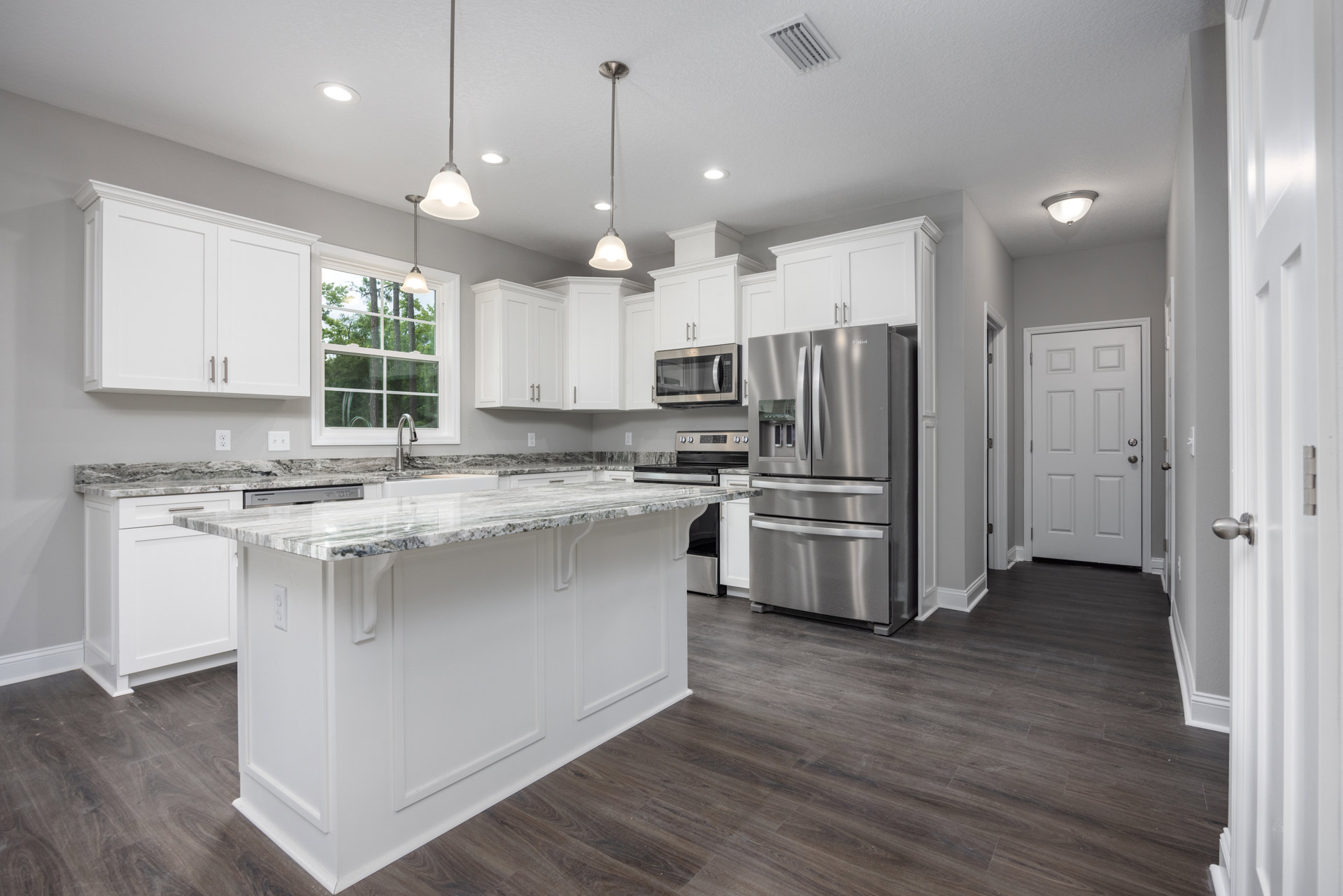 Spacious kitchen featuring a large central island with quartz countertop, stainless steel refrigerator and freezer, built-in microwave with glass door, white cabinetry, modern