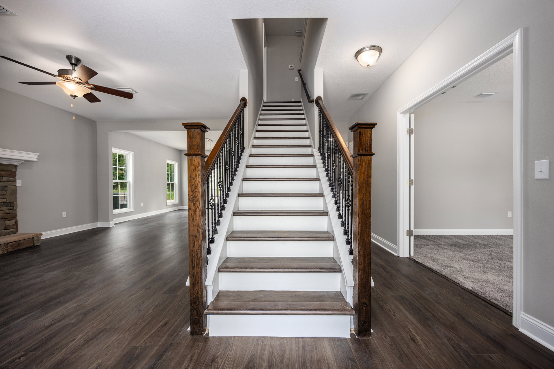Wood staircase with matching handrails and laminate floors, stone accent wall, ceiling fan with light fixture, and light switch on plaster wall