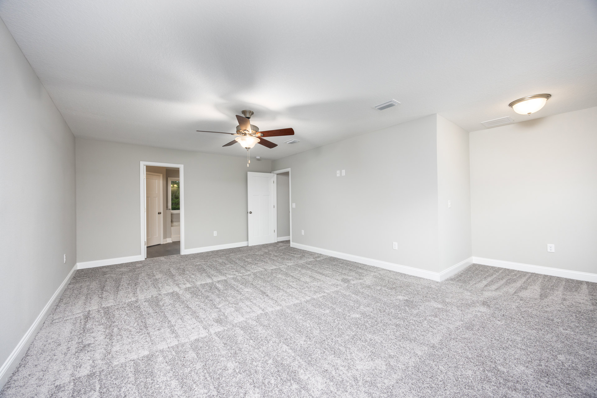 Carpeted bedroom with white walls, ceiling fan with light fixture, open white door revealing bathroom with bathtub