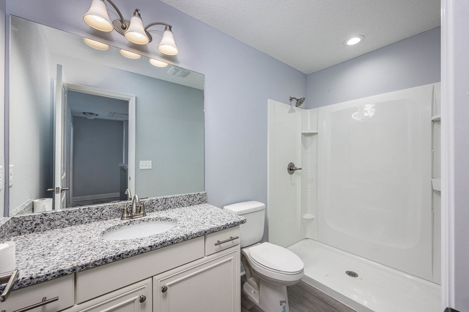 Bathroom with white tile shower, marble countertop vanity, undermount sink, chrome faucet, wall-mounted mirror, recessed ceiling lights, and toilet with toilet paper holder.