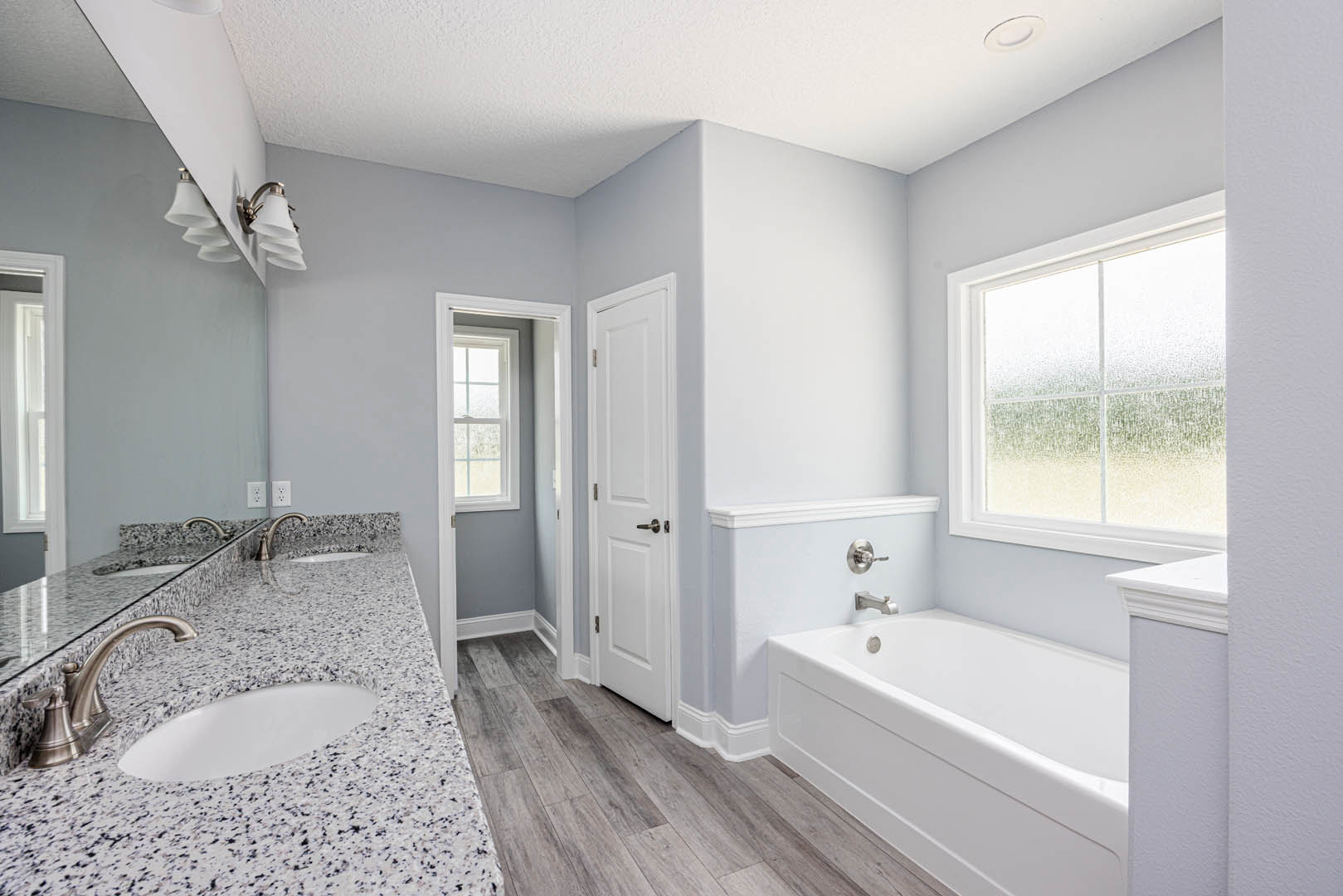 Marble countertop with chrome faucet and white sink, freestanding bathtub beside frosted glass window, light tile walls and floor