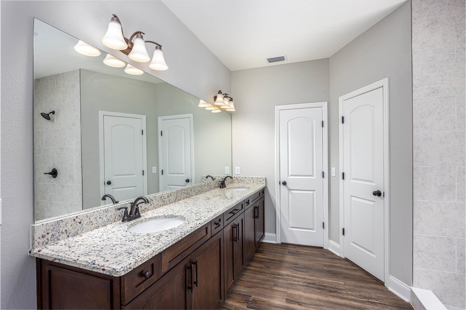 Bathroom with double vanity featuring undermount sinks, wide framed mirror, white cabinetry, black hardware, wood flooring, and white door with black handle