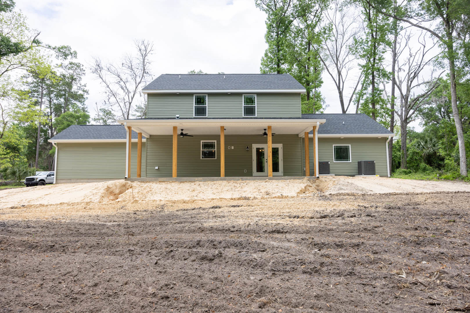 Single-story house with white-framed windows and covered porch, surrounded by a large dirt yard, sparse trees, and clear sky