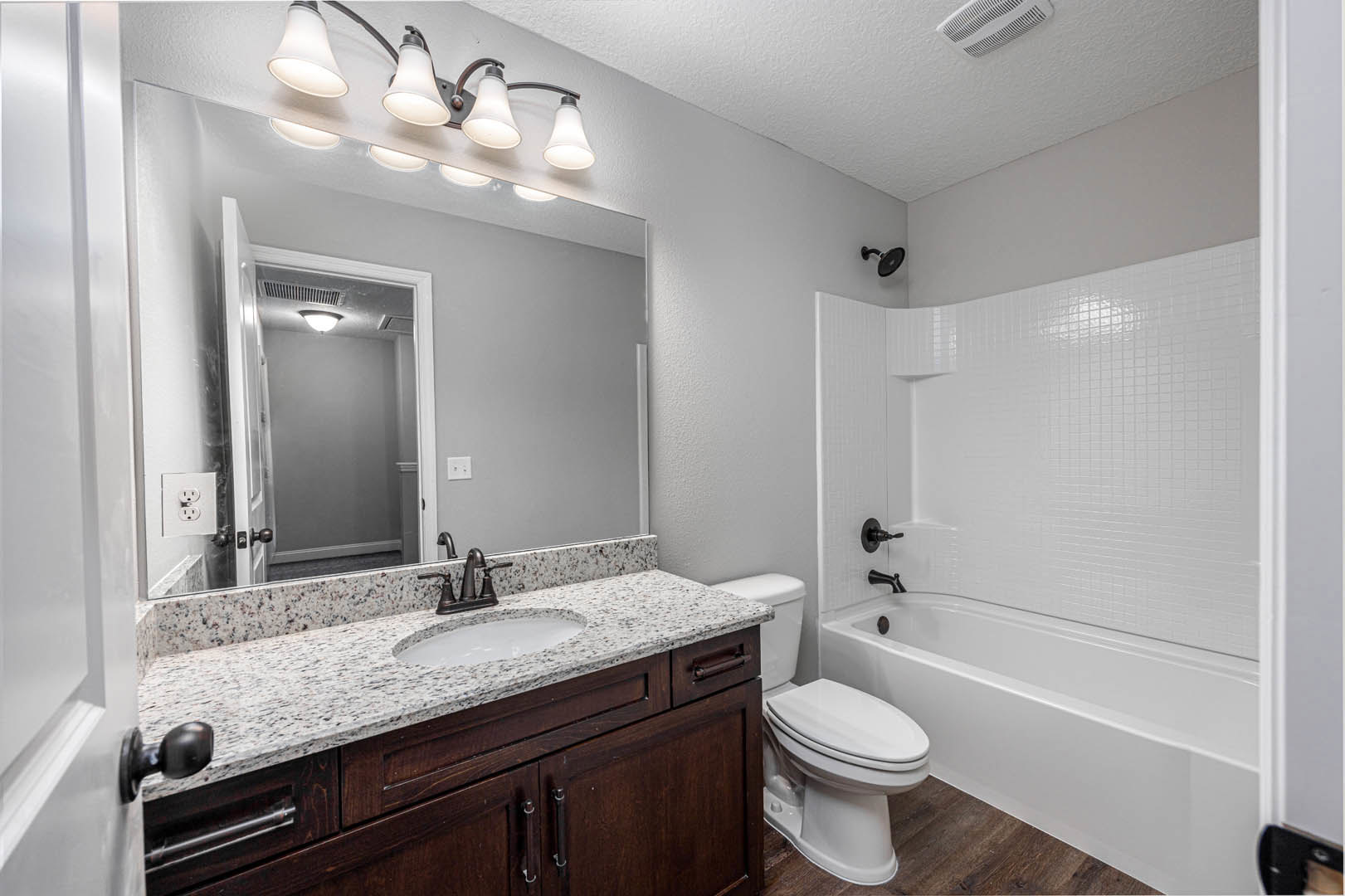 Modern bathroom featuring a freestanding bathtub, white sink with chrome faucet, light gray tile flooring, wood cabinetry, row of ceiling lights, and a white toilet with lid