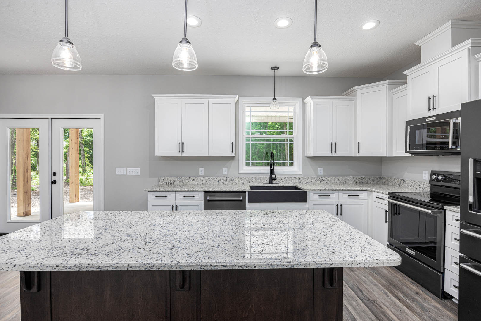 White kitchen cabinets with granite countertops, black base island, open microwave door, window with white frame, double glass-paneled doors, black oven with silver handle