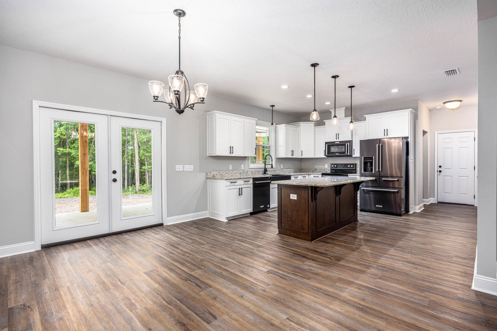 Open kitchen and dining area with wood flooring, stainless steel refrigerator with glass door, white cabinetry, double glass-paneled doors, white door with black knobs, close-up