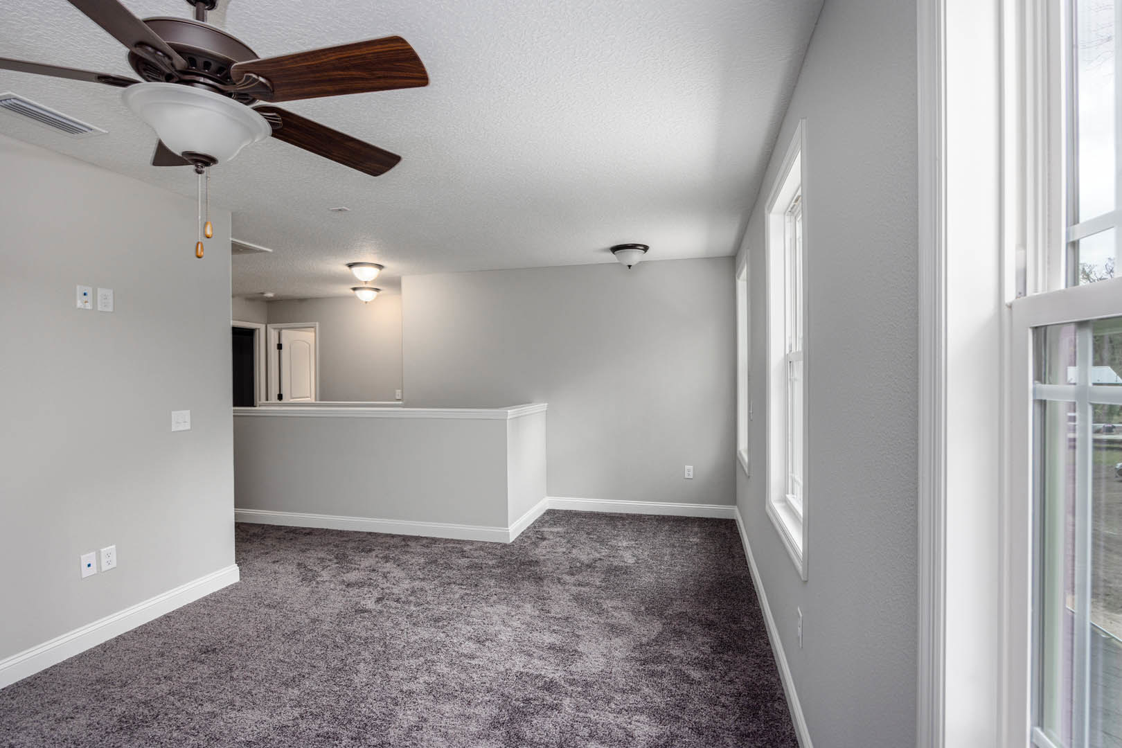 Neutral-toned carpeted room with white ceiling, central ceiling fan and light fixture, plain walls, and minimal decor