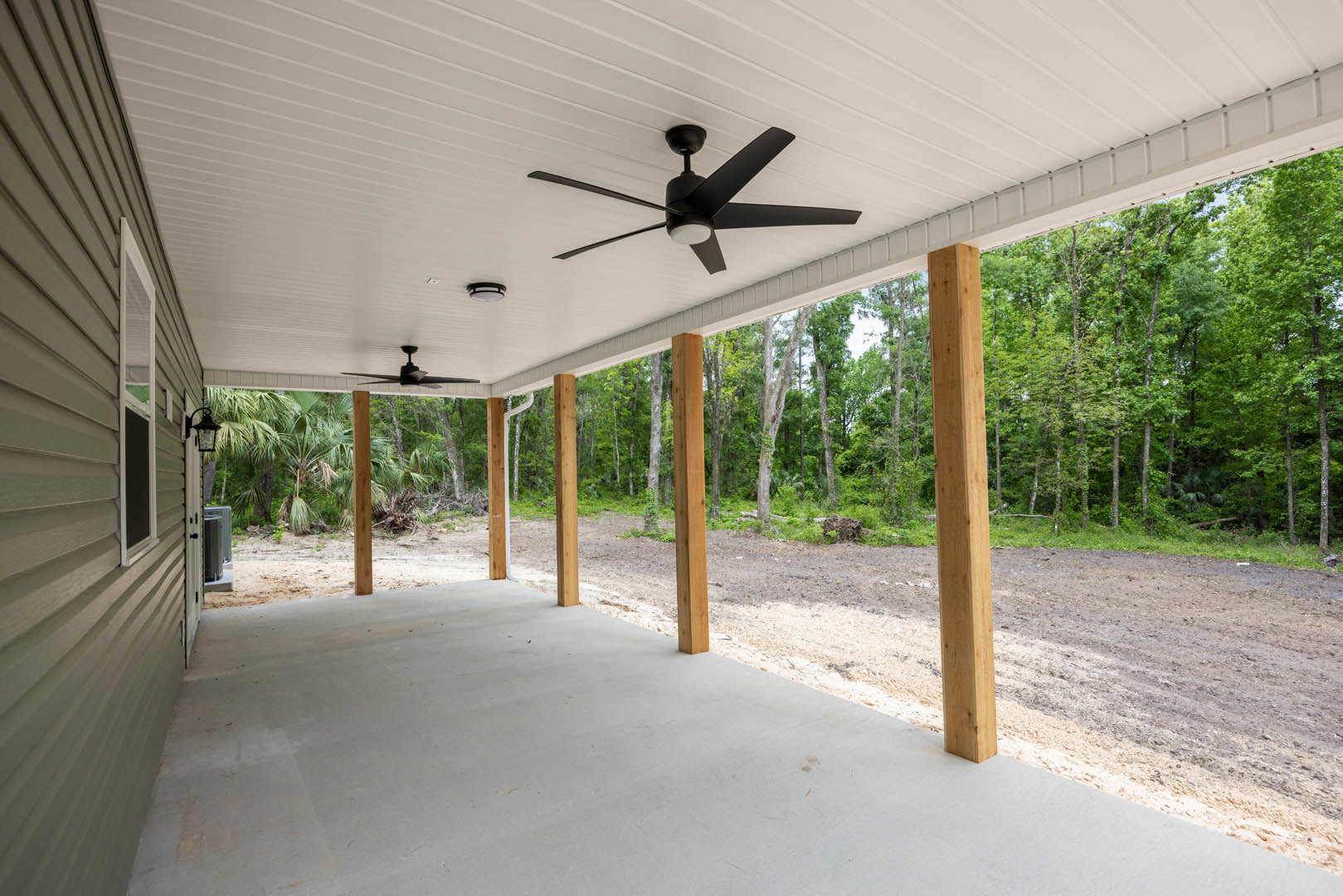 Concrete porch with wooden pillars, ceiling fans, and a leafy tree visible in the background