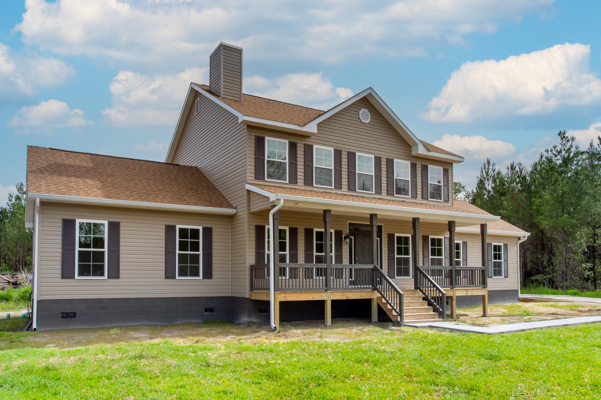 Two-story house with white-framed windows, covered porch with stairs, brick chimney, and green lawn under a cloudy sky