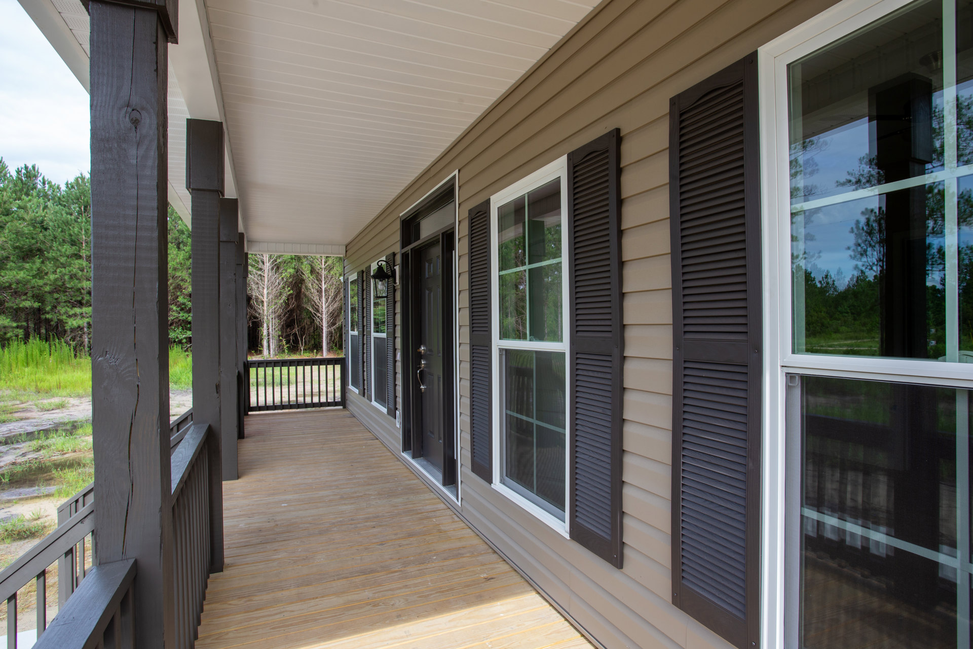 White siding house with covered front porch, wood deck, large windows, glass door, and surrounding trees