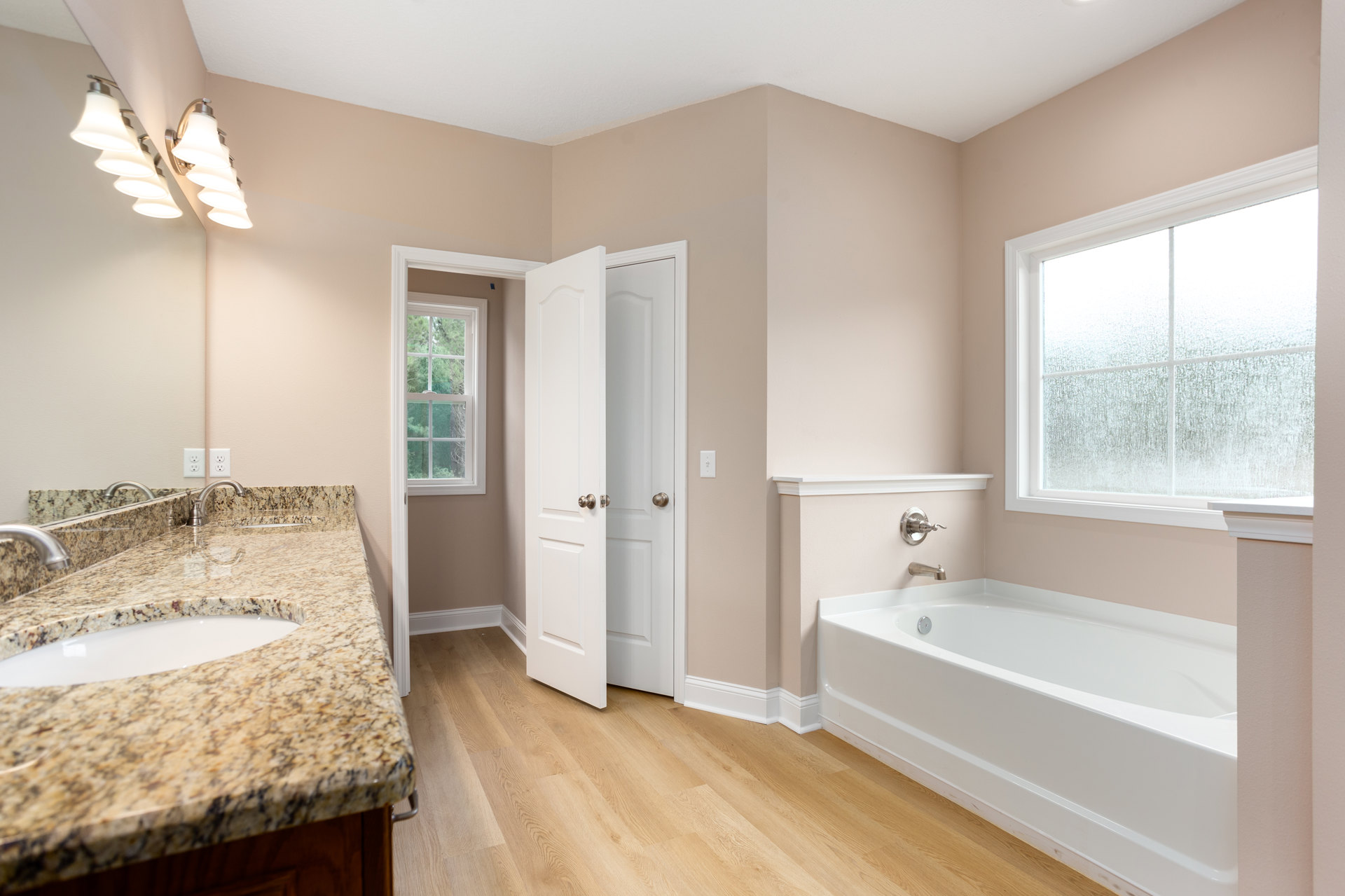 Bathroom with marble countertop, dual sinks, white freestanding bathtub with chrome faucet, frosted glass window in white frame, tiled floor and walls, close-up of metal knob