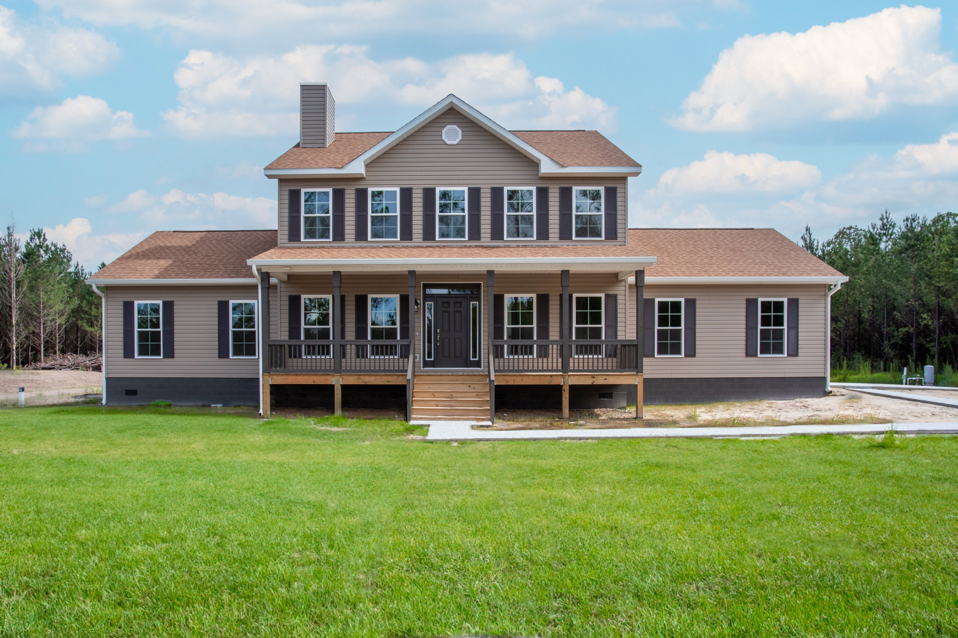 Expansive two-story home with white-framed windows, black glass-paneled front door, wooden porch steps, and manicured green lawn under a partly cloudy sky