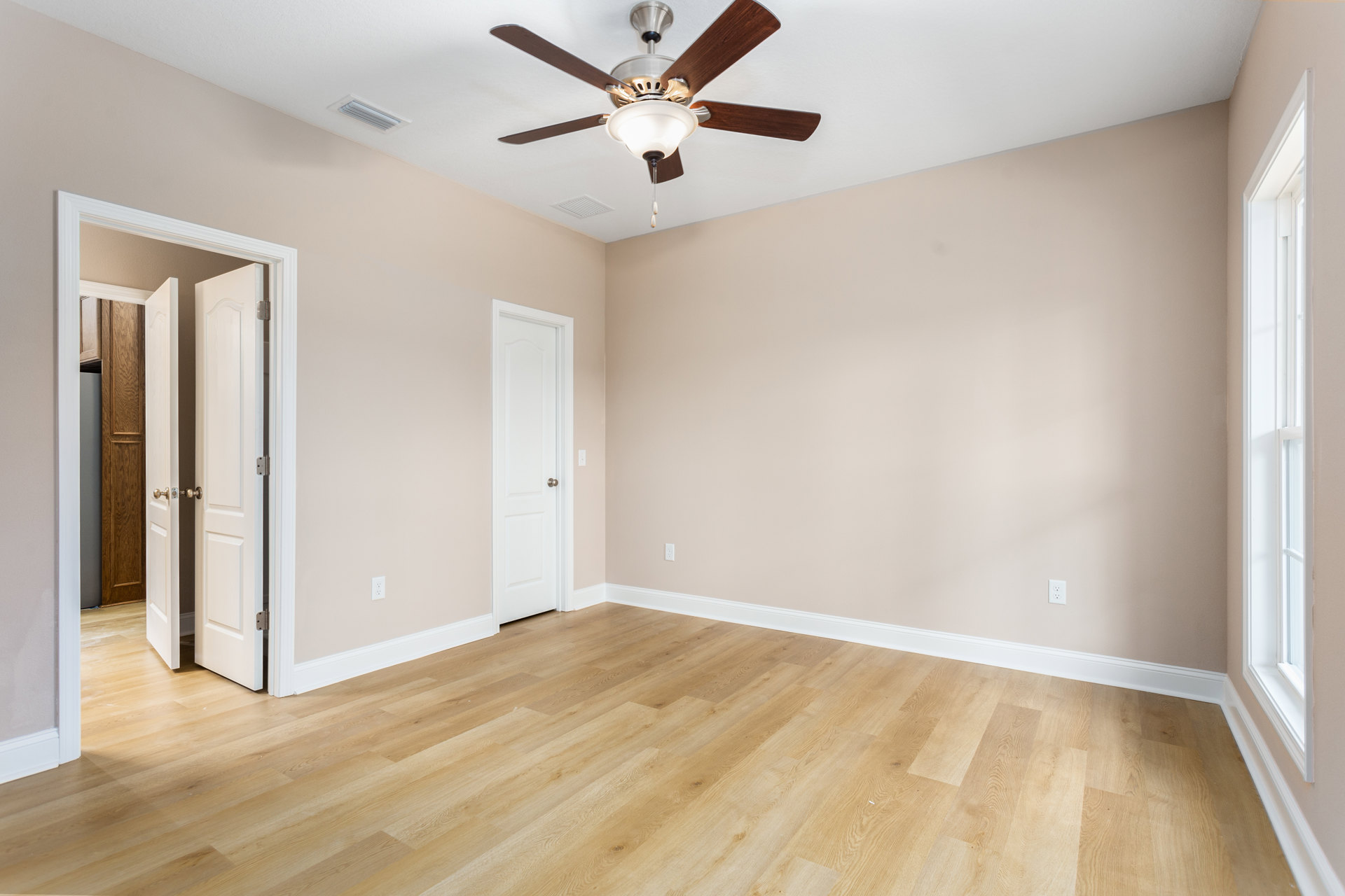 Ceiling fan with light fixture mounted on white plaster ceiling, wood flooring with white baseboard trim, white door with round knob and visible hinge, close-up window in