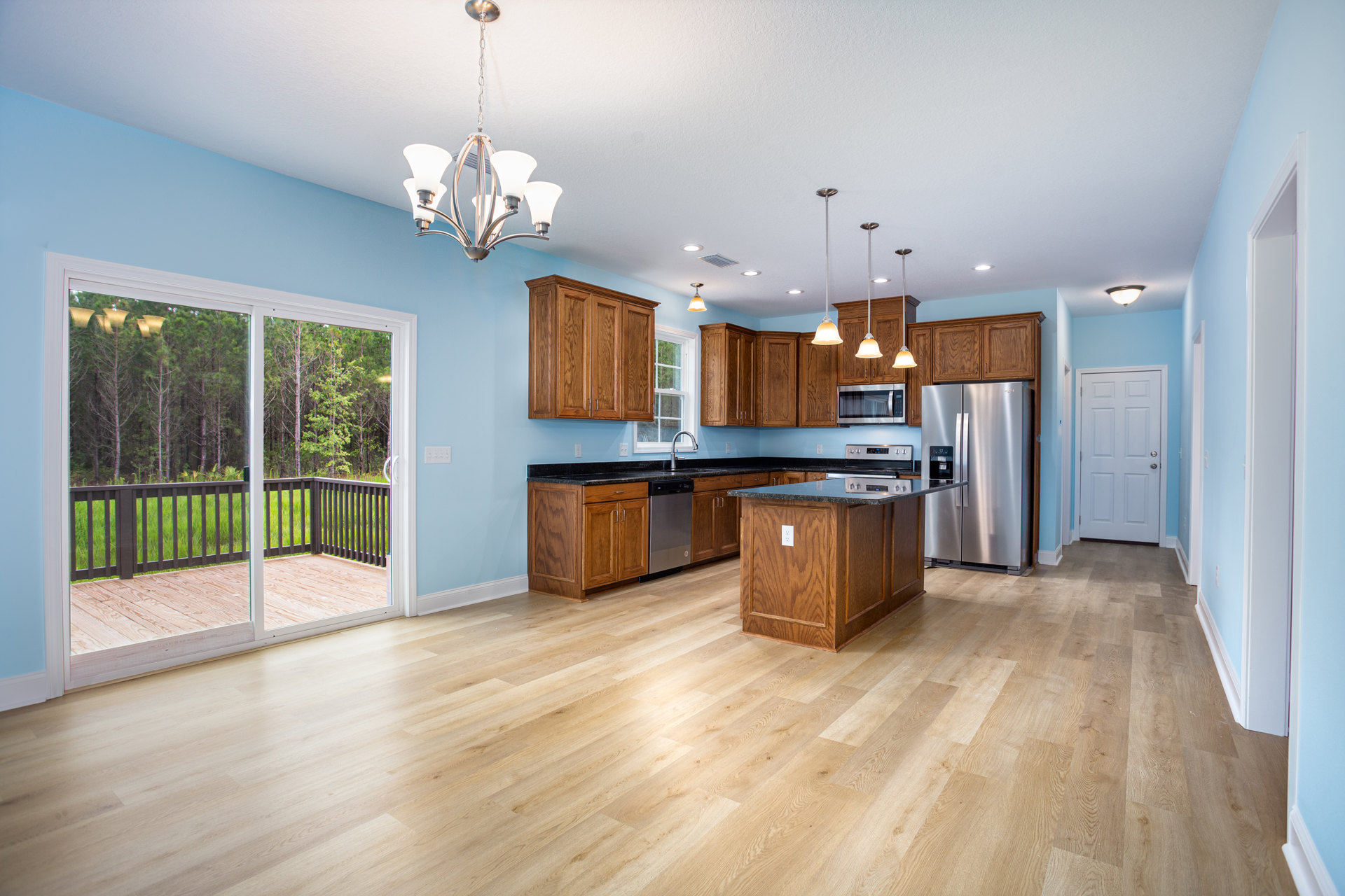 Kitchen with hardwood floor, light blue wall, silver refrigerator with black handle, white door with silver handle, microwave oven, close-up chandelier, view of deck with fence and