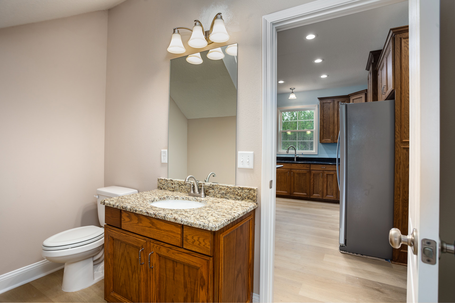 Bathroom with tile flooring, white toilet, sink and cabinet, refrigerator beside countertop, window above faucet, neutral wall finishes