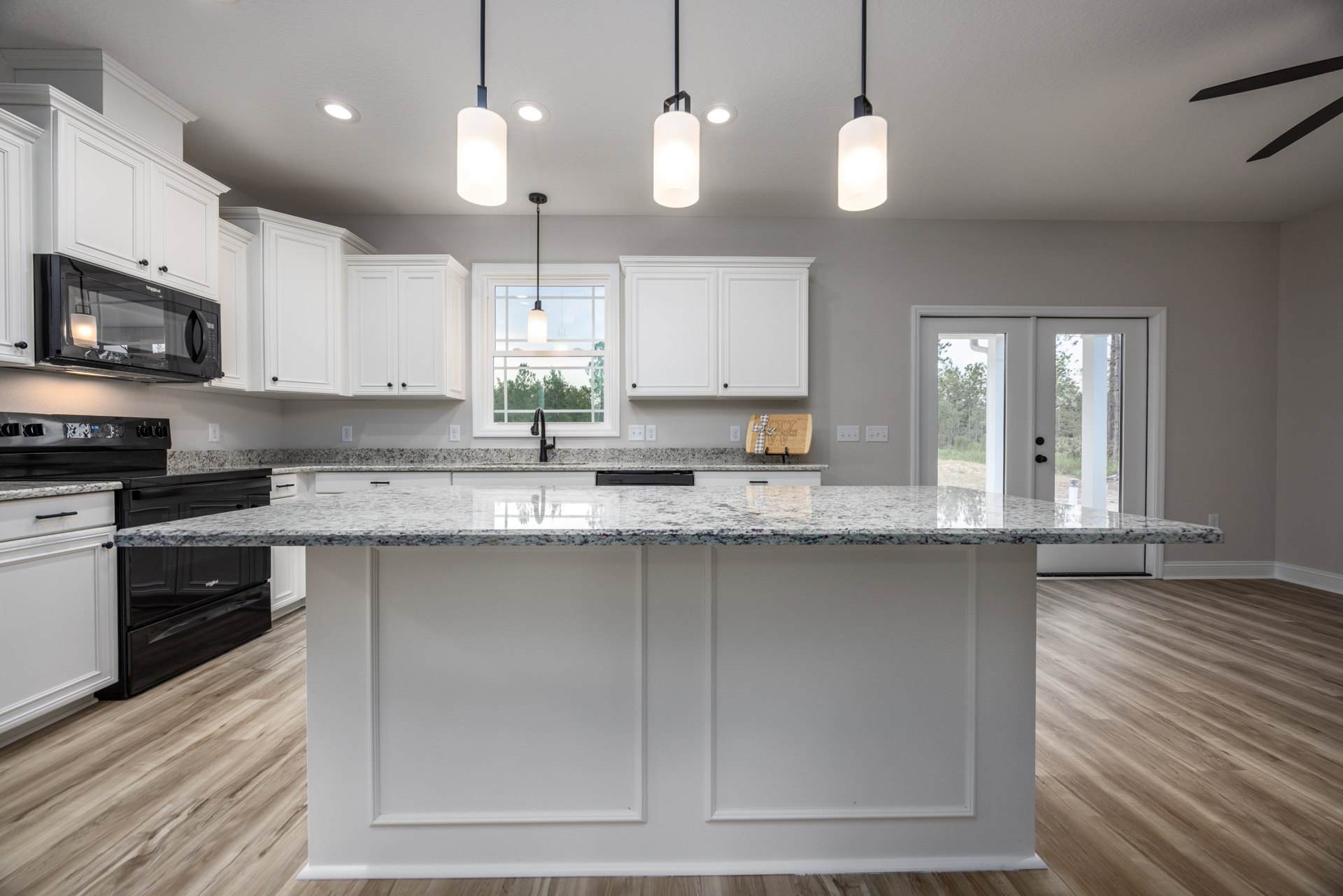 Marble kitchen countertop with white cabinetry, stainless sink, black microwave, and overhead lighting against a white wall