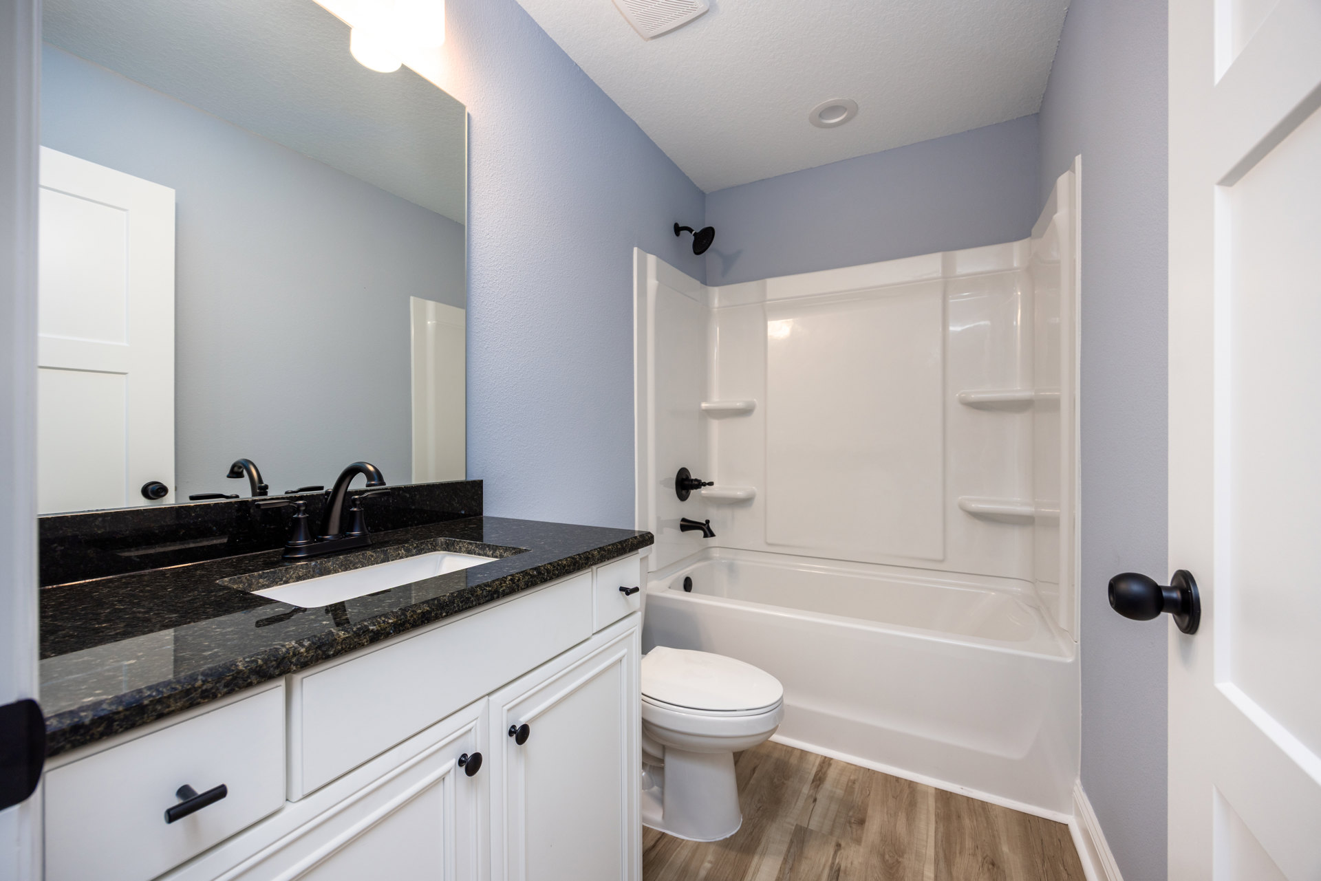 White freestanding bathtub and matching sink on tiled floor, white toilet with closed lid, chrome faucet, light reflecting off smooth surfaces, neutral cabinetry and countertop.