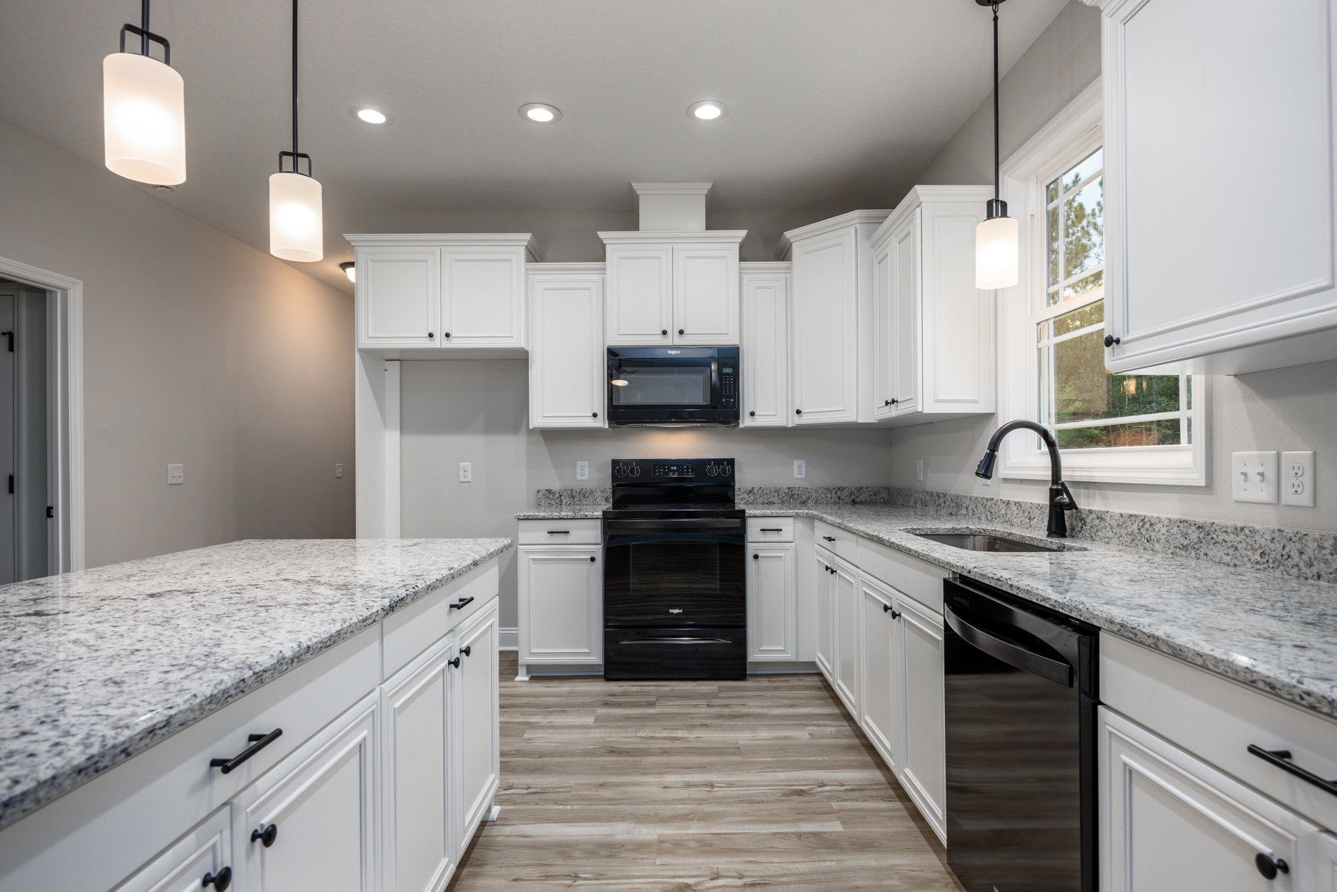 White kitchen cabinets with granite countertops, black oven and refrigerator, stainless steel microwave being opened, black metal handles, close-up of ceiling light fixture.