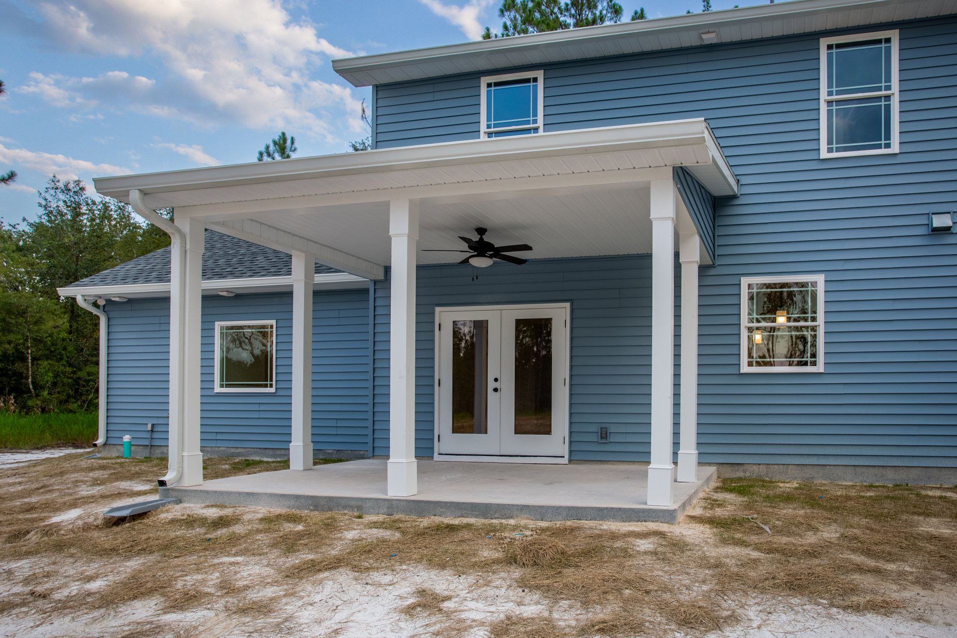 Blue siding exterior with double glass doors, white-framed windows, covered porch, and white ceiling fan with light fixture.