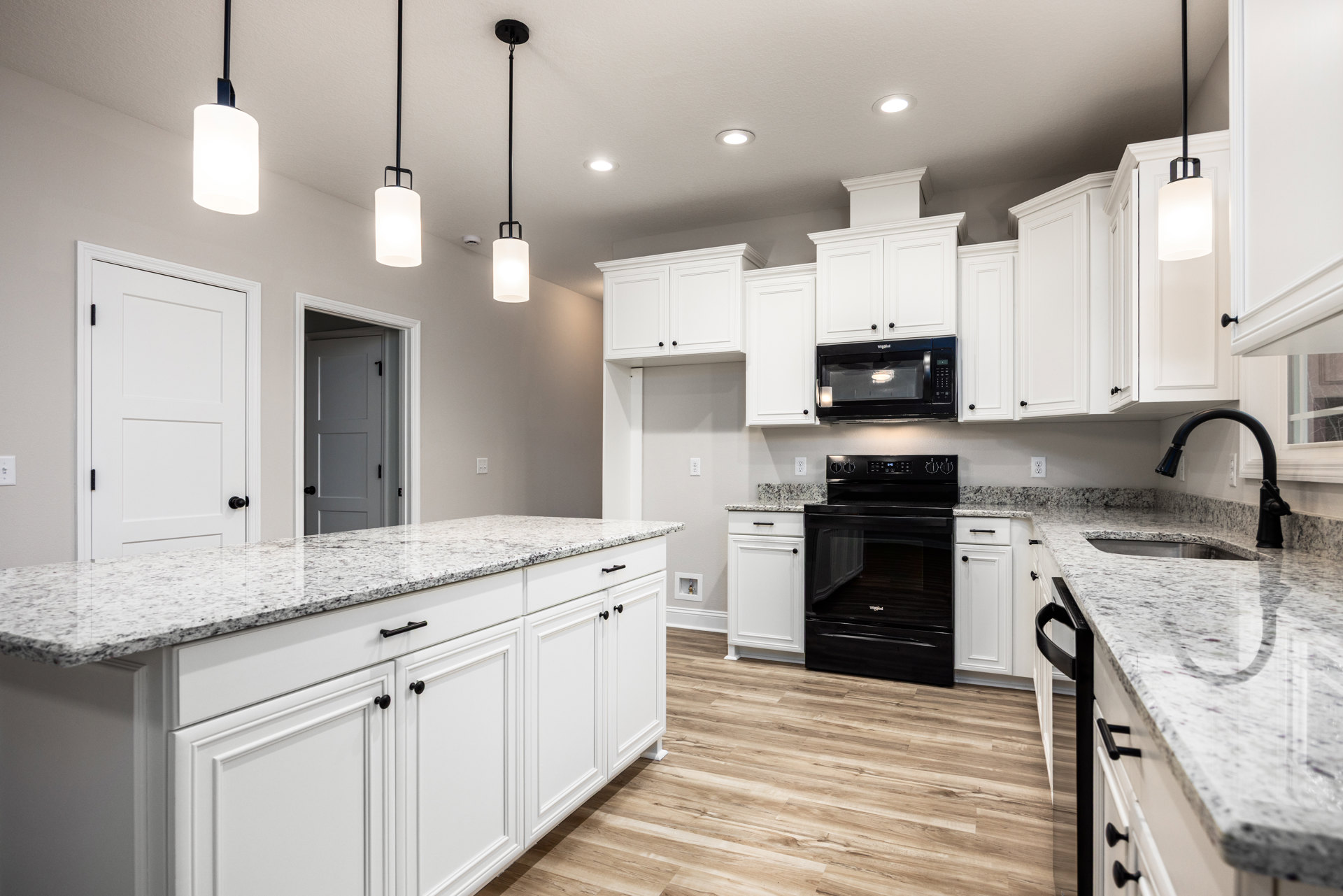 White kitchen cabinets with black appliances including a stove and microwave, white countertop, and a light fixture with a white shade.