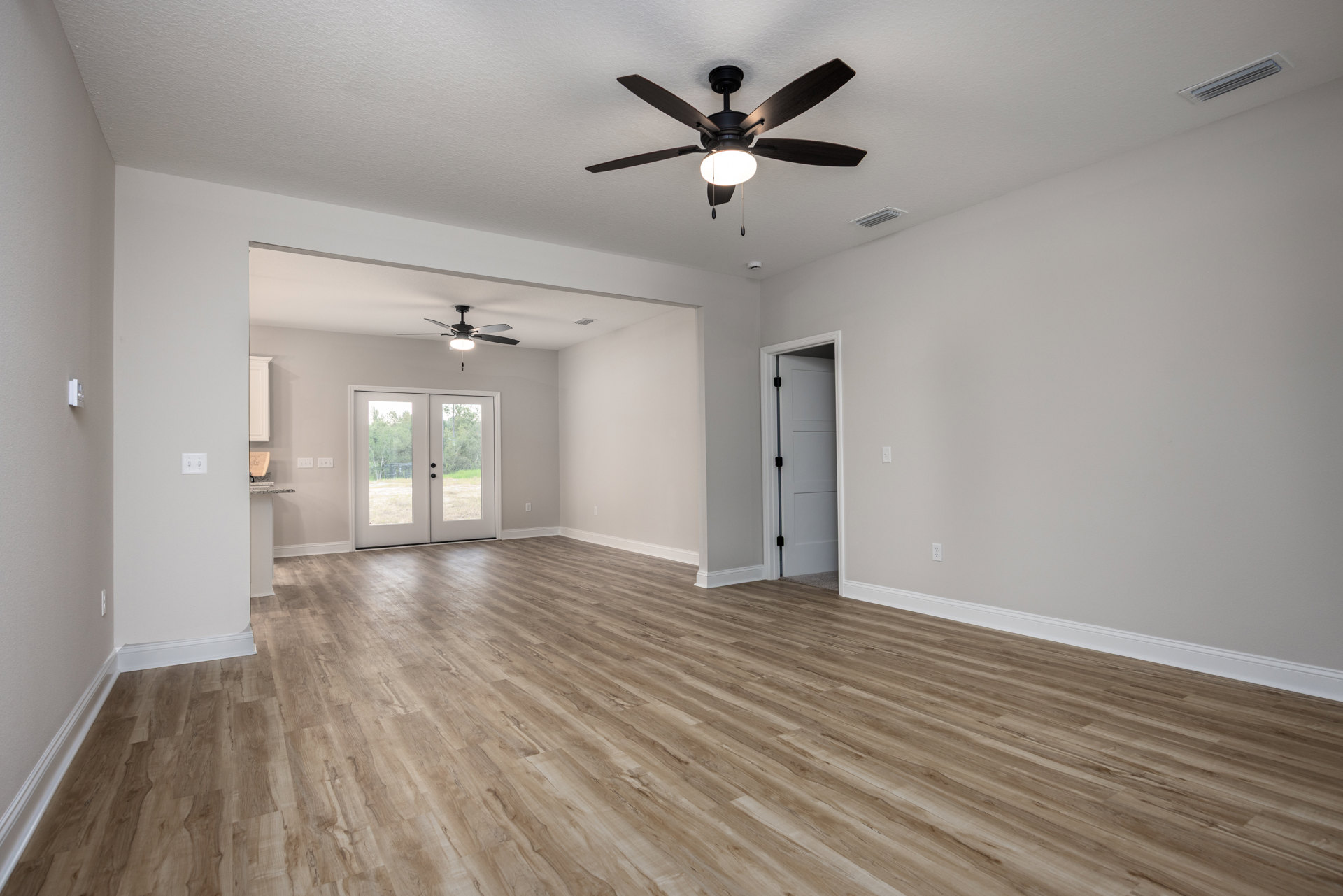 Wood flooring and white walls in a bright room with a ceiling fan, double glass-paneled doors, and a white door with a black lock.