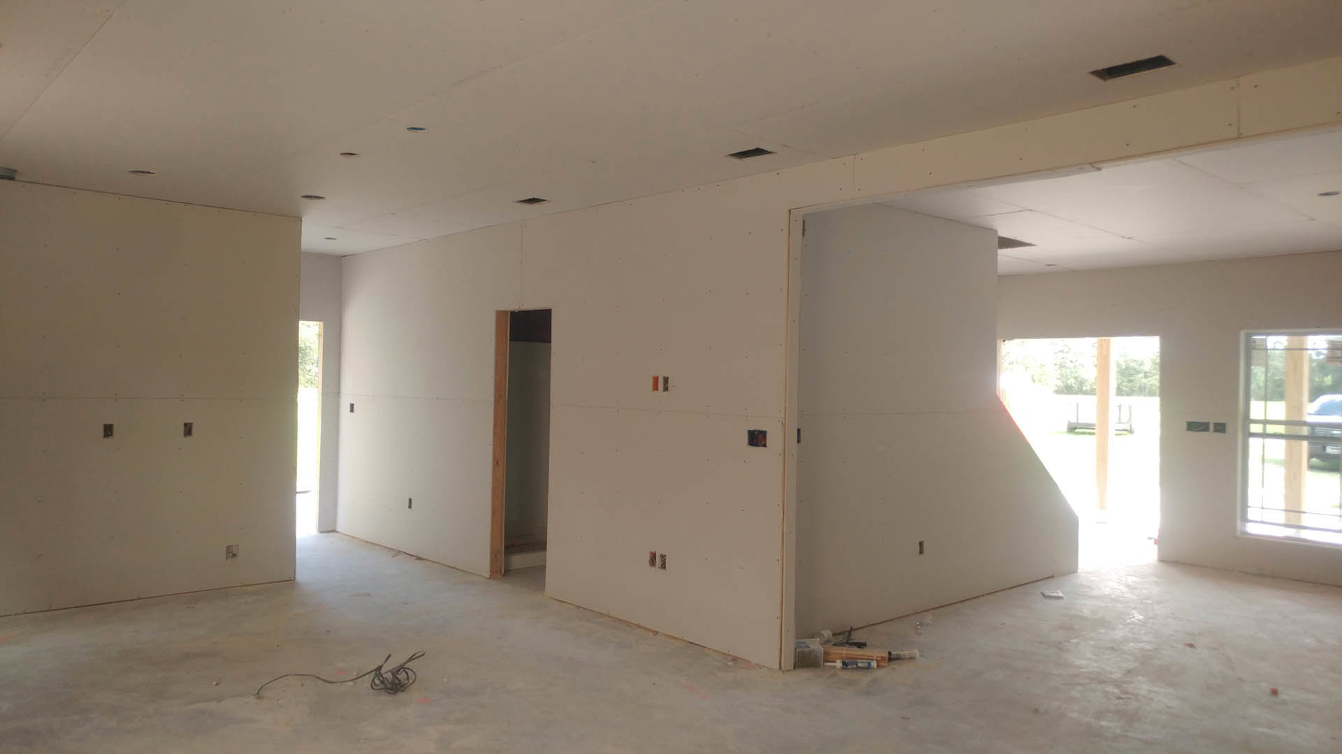 White plaster walls and ceiling, wood flooring, single-panel door with brushed metal handle, open doorway leading to adjacent room, natural light filtering in, minimal interior