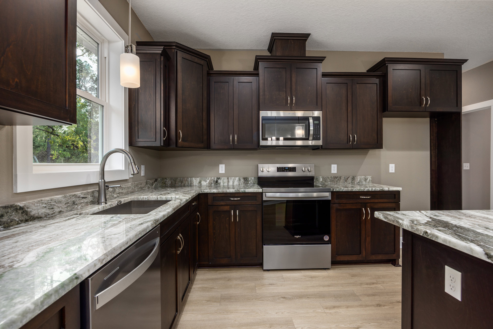 Kitchen with dark wood cabinets, granite countertops, stainless steel appliances, built-in microwave, oven, sink with chrome faucet, and white electrical outlet on marble surface