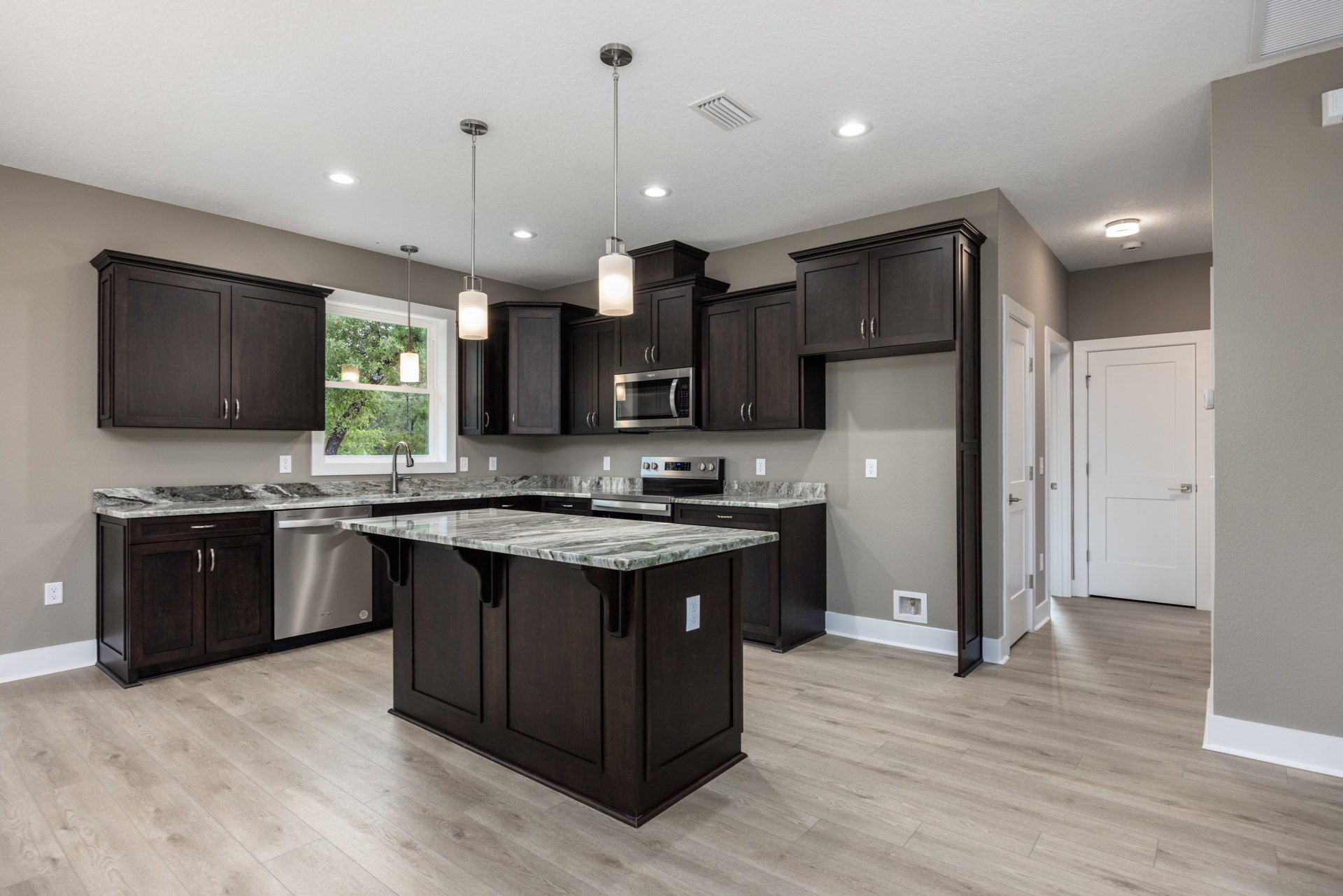 Kitchen with dark wood cabinets, marble island countertop, stainless steel microwave, white door with silver handle, and metal support pole