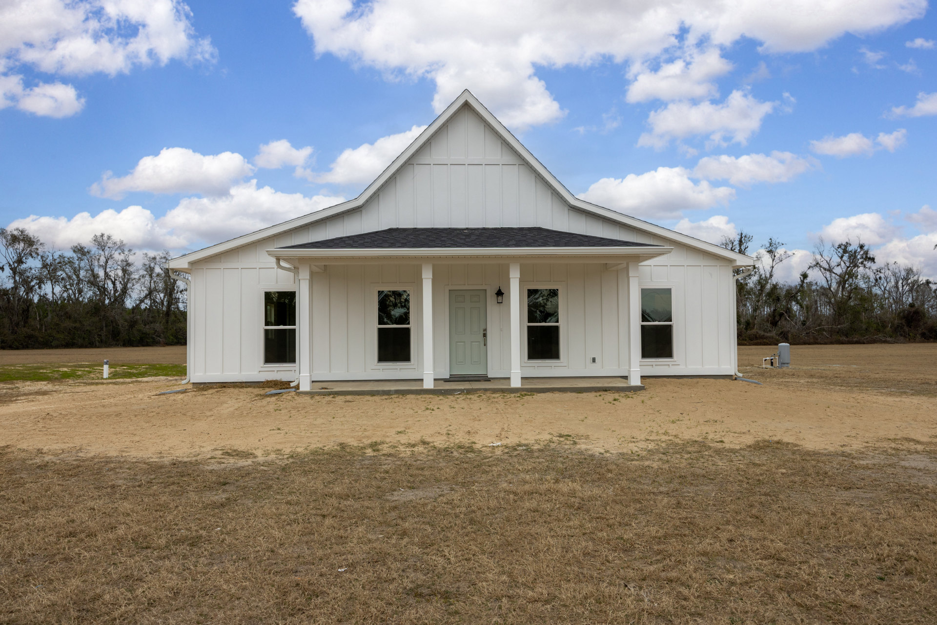White house with gable roof, white door, and glass windows, set on a dirt lot under a clear blue sky.