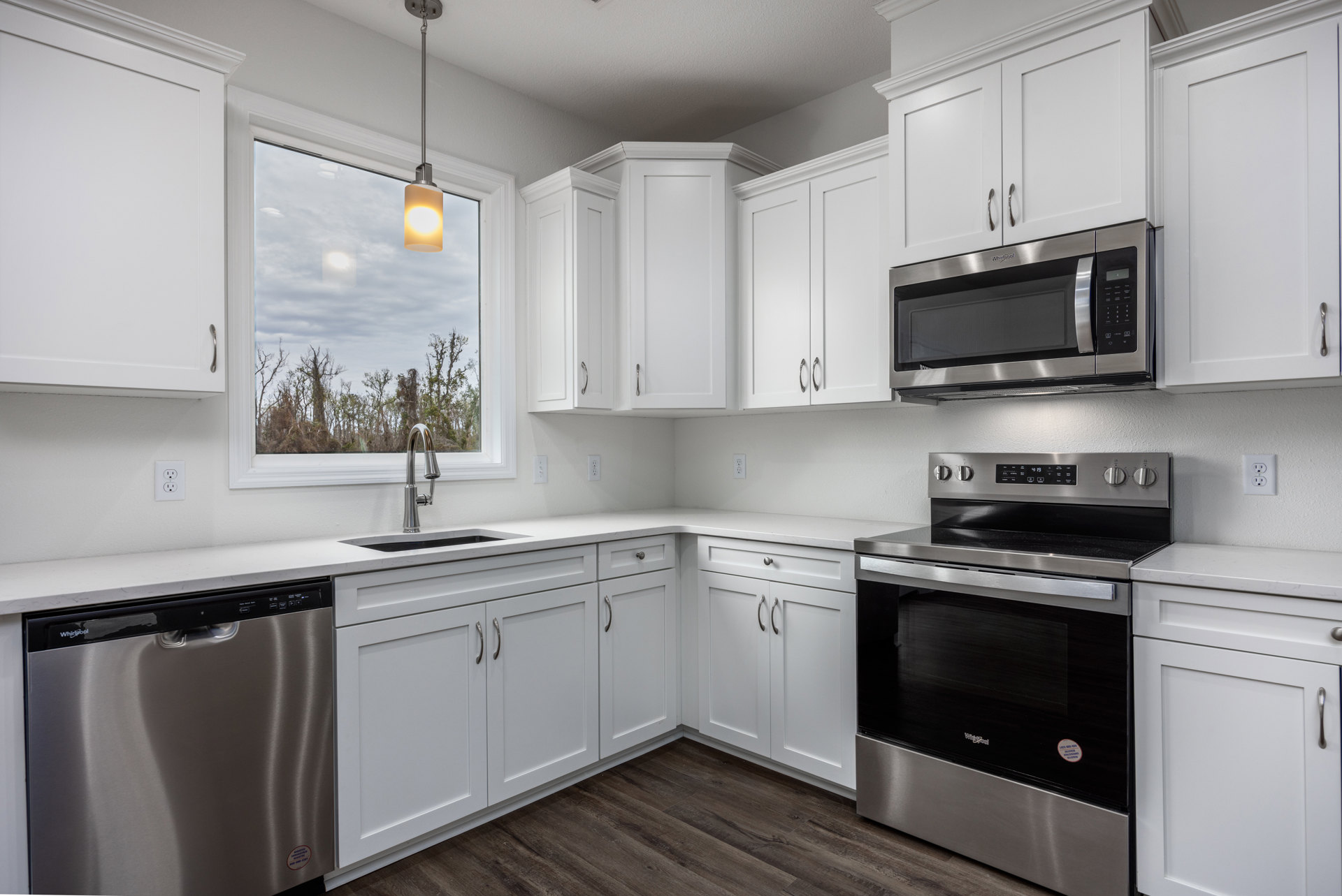 White kitchen cabinets, stainless steel oven with black glass door, built-in microwave, silver dishwasher, stone countertop, window providing natural light, modern fixtures
