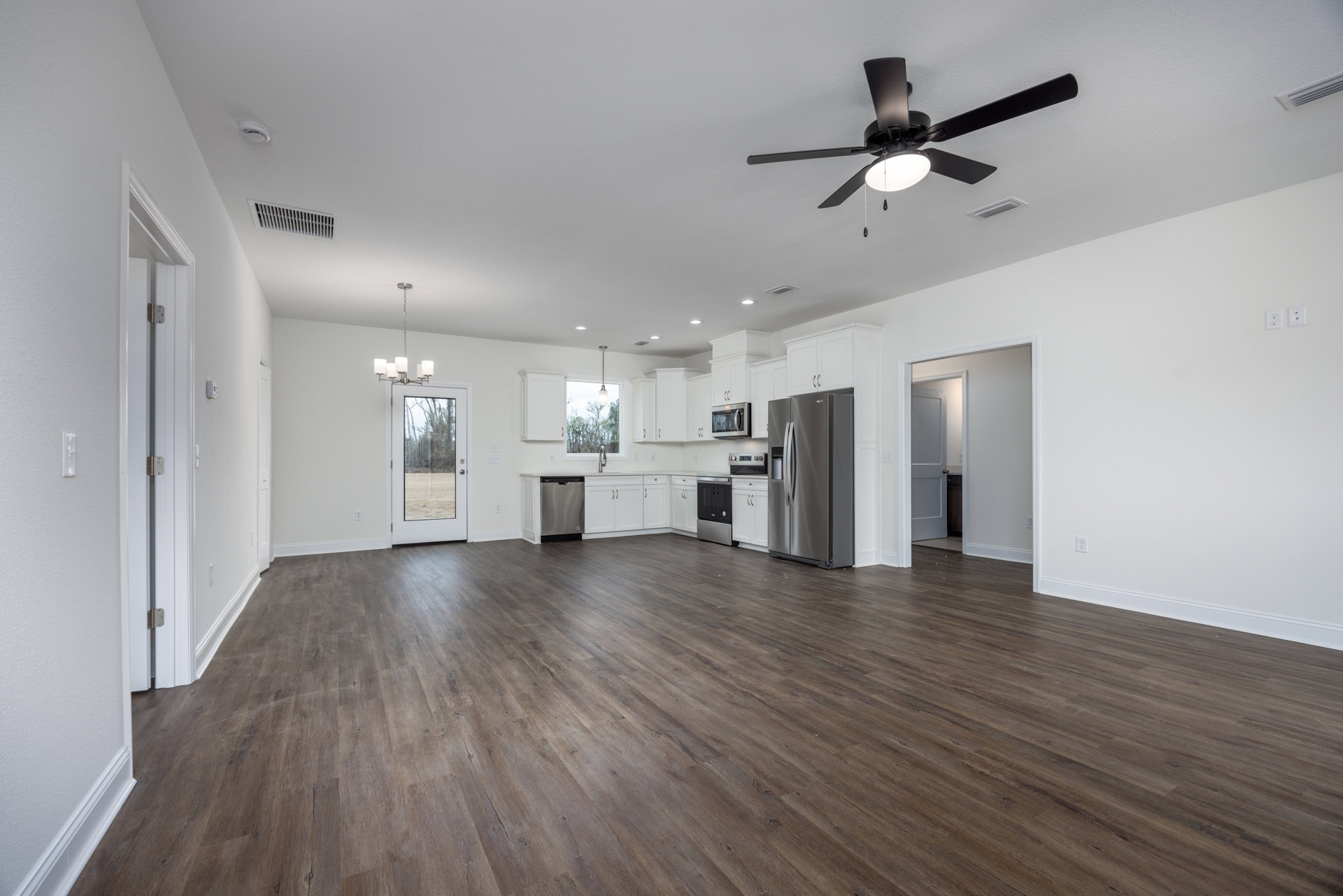 Spacious kitchen with wood flooring, stainless steel refrigerator, built-in microwave, ceiling fan with light, and glass door overlooking backyard
