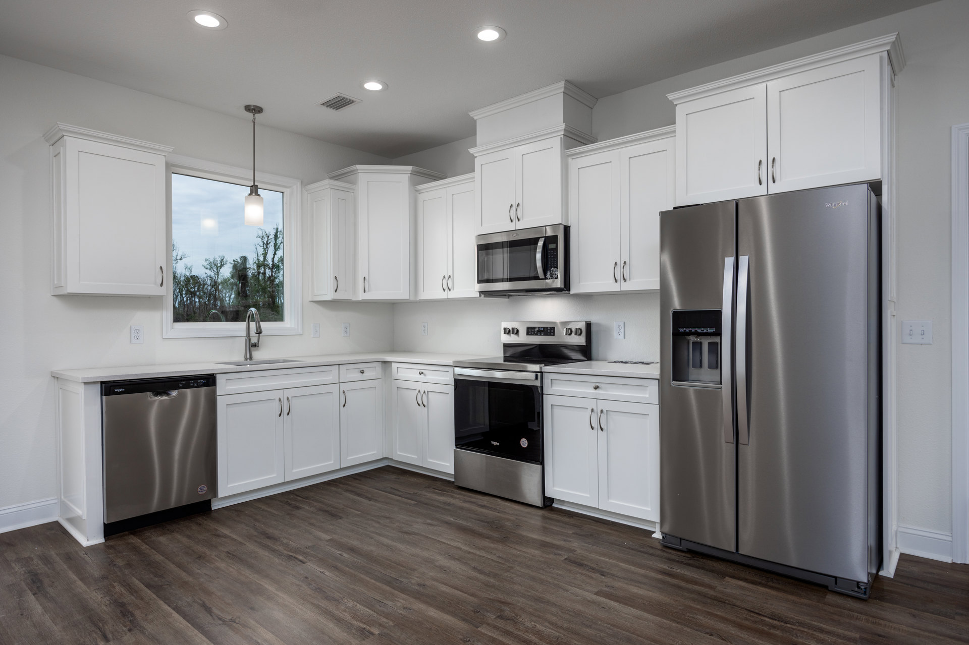 White kitchen cabinets, stainless steel refrigerator with ice and water dispenser, built-in microwave, silver dishwasher with black handle, stainless steel oven and stove, light