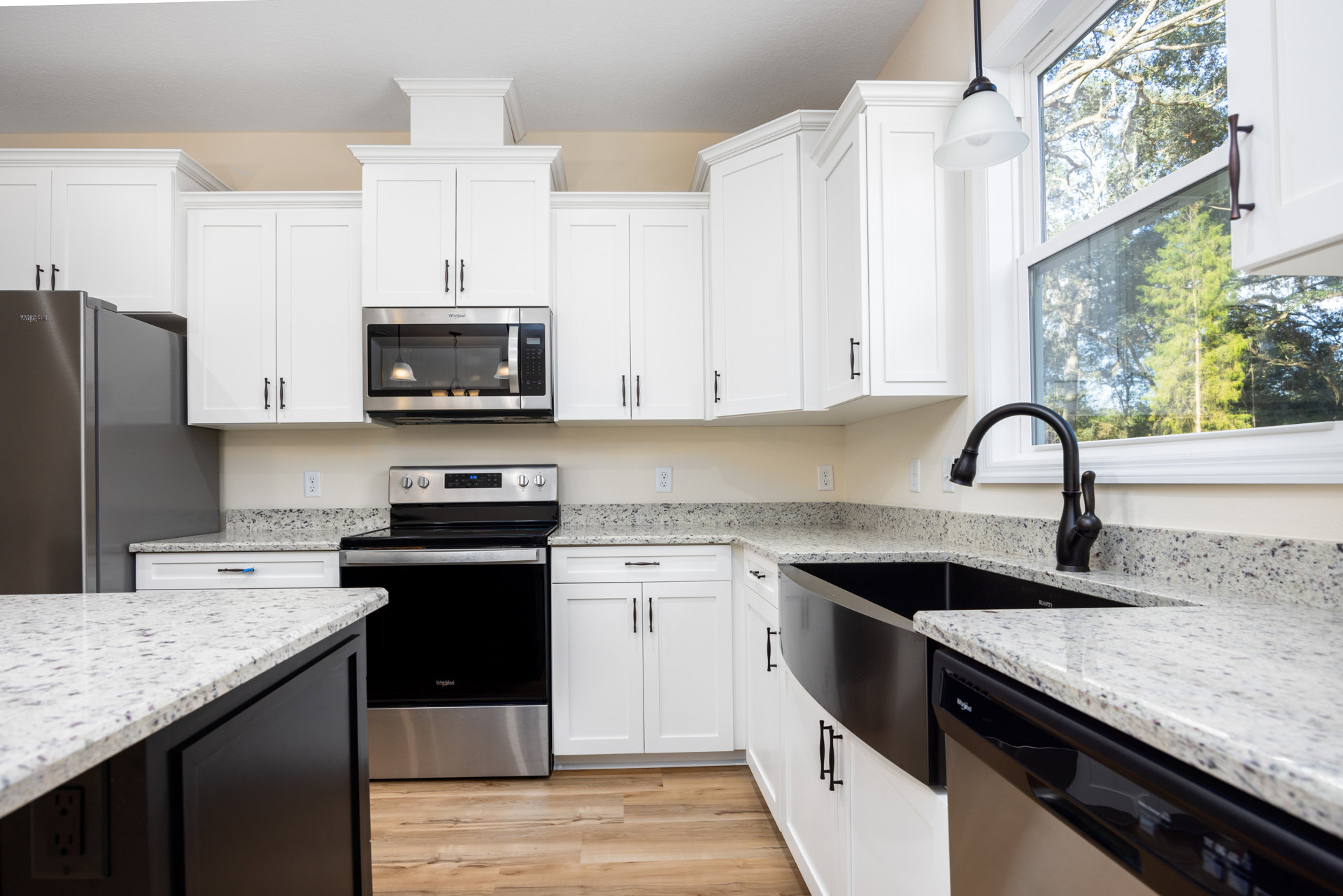 White kitchen cabinets, black appliances including oven and refrigerator, white and black countertops, microwave with illuminated window, white light fixture with black pole.