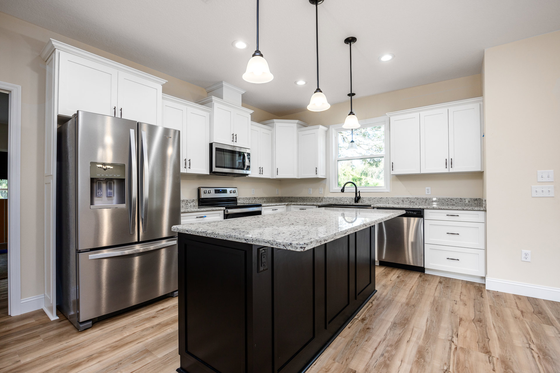 Spacious kitchen featuring a granite island with seating, stainless steel refrigerator with ice and water dispenser, open microwave oven, white cabinetry with black handles, and